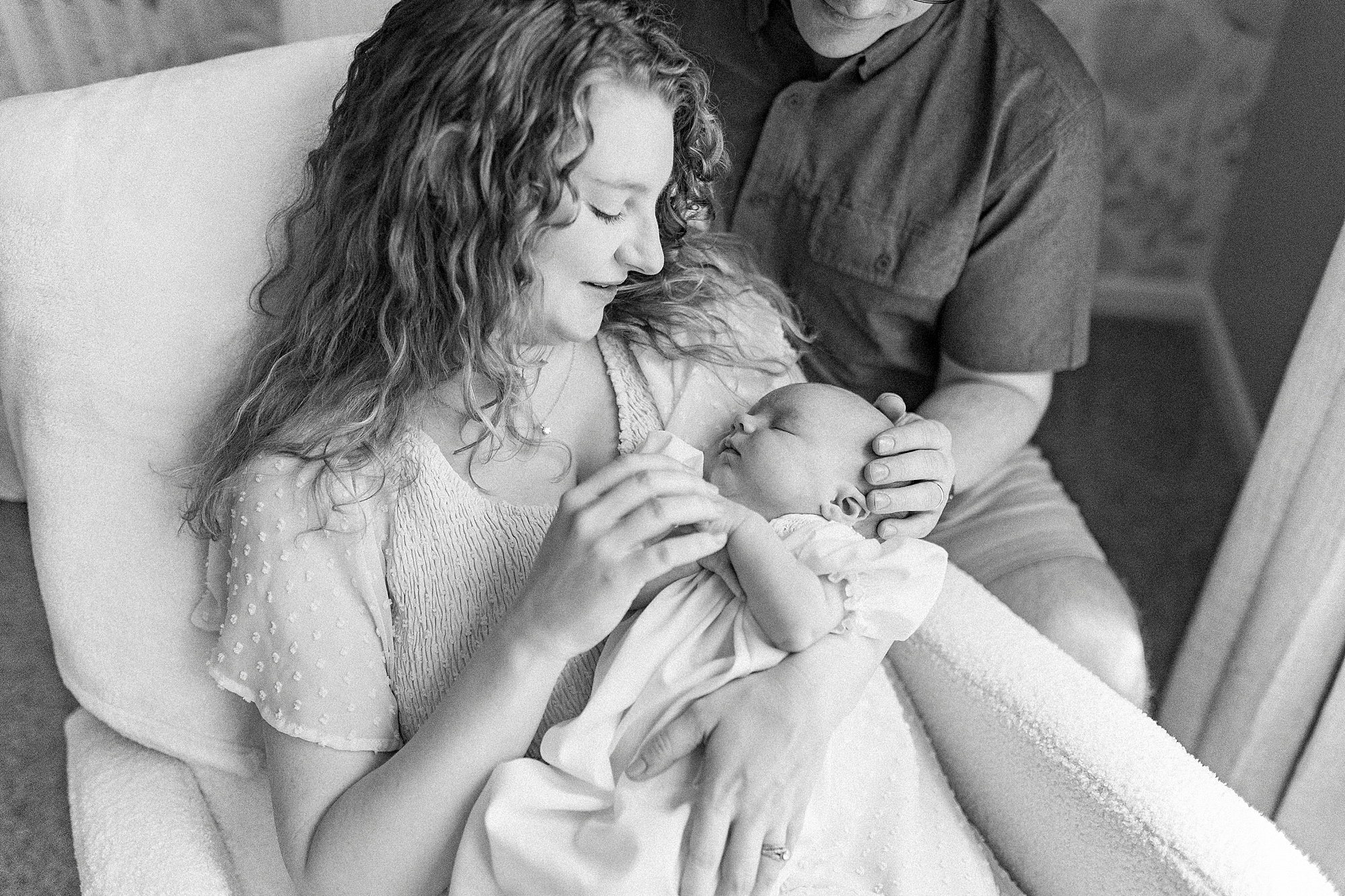 mom snuggles baby in rocking chair with dad next to them