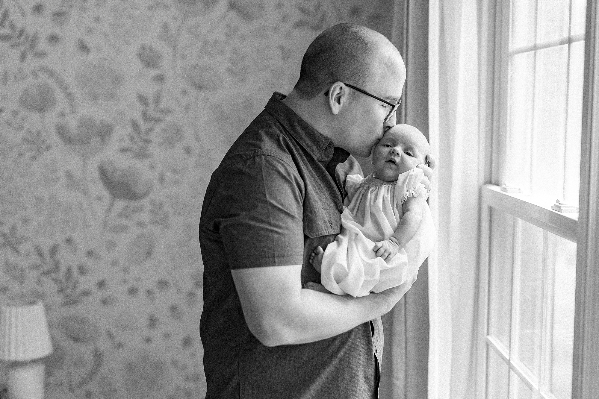 dad kisses baby girls' forehead during lifestyle newborn session with Winston-Salem family photographer