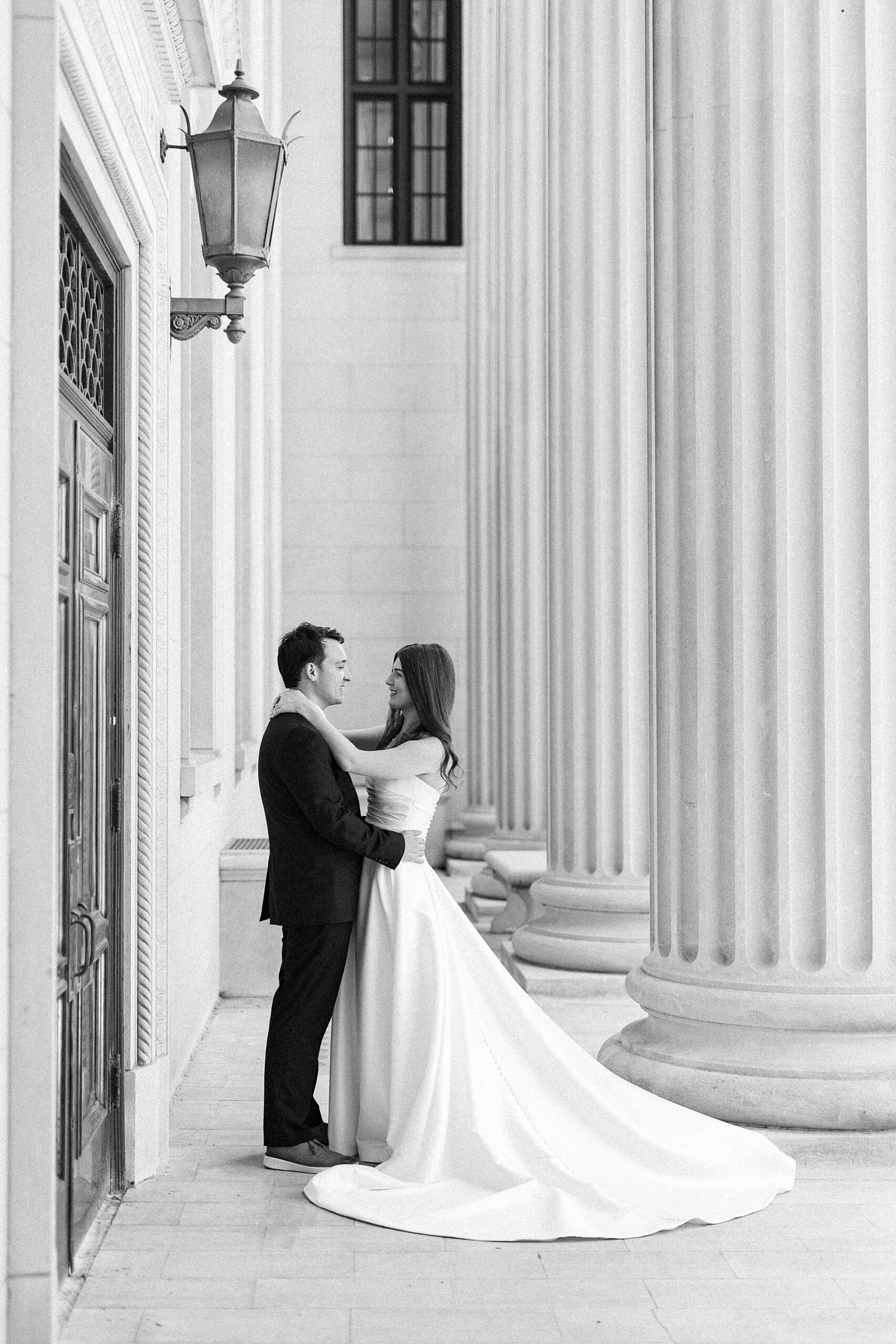 bride and groom hug between pillars at building in Uptown Charlotte 