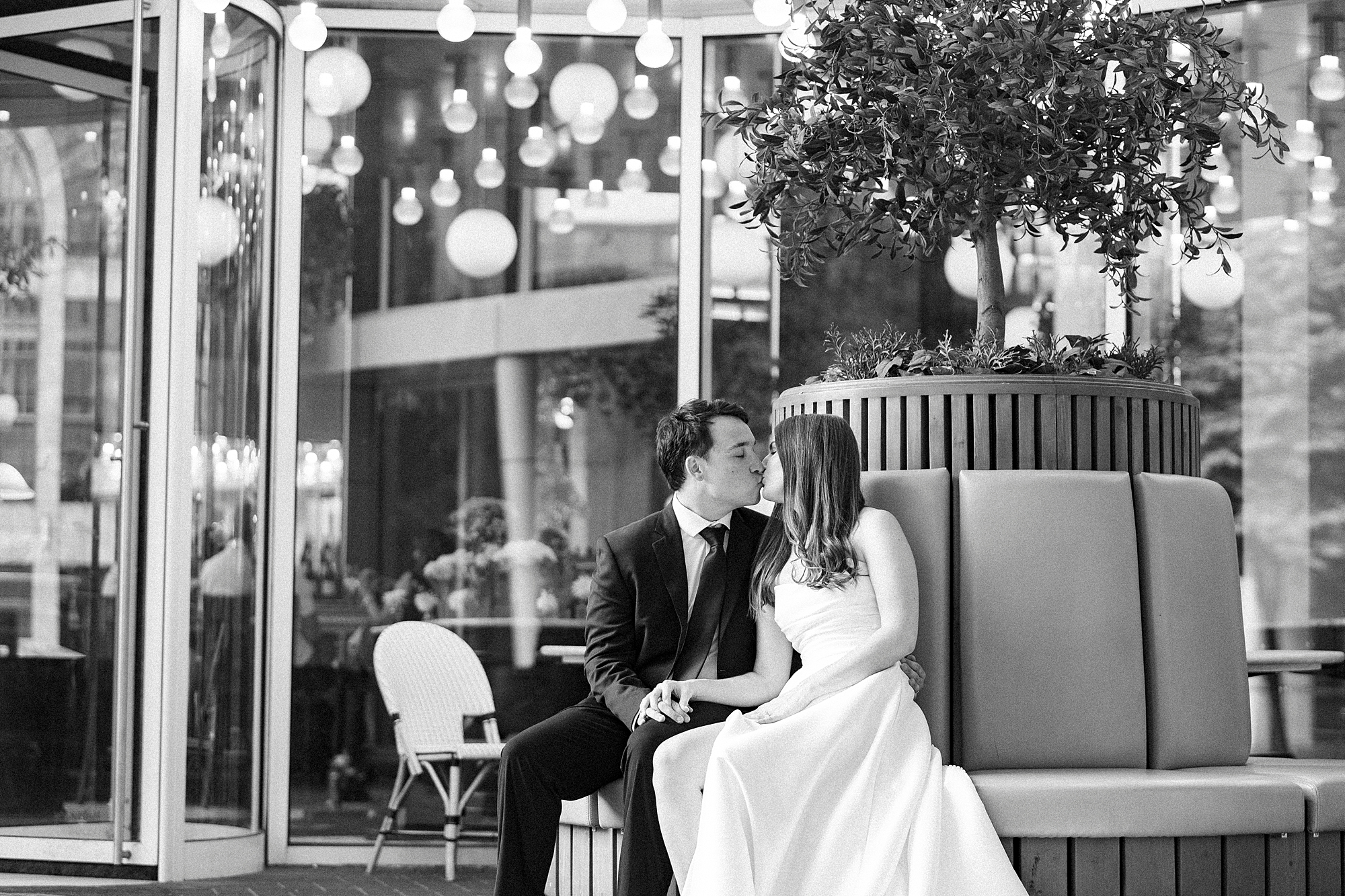 man and woman sit on bench kissing inside French restaurant in Charlotte NC