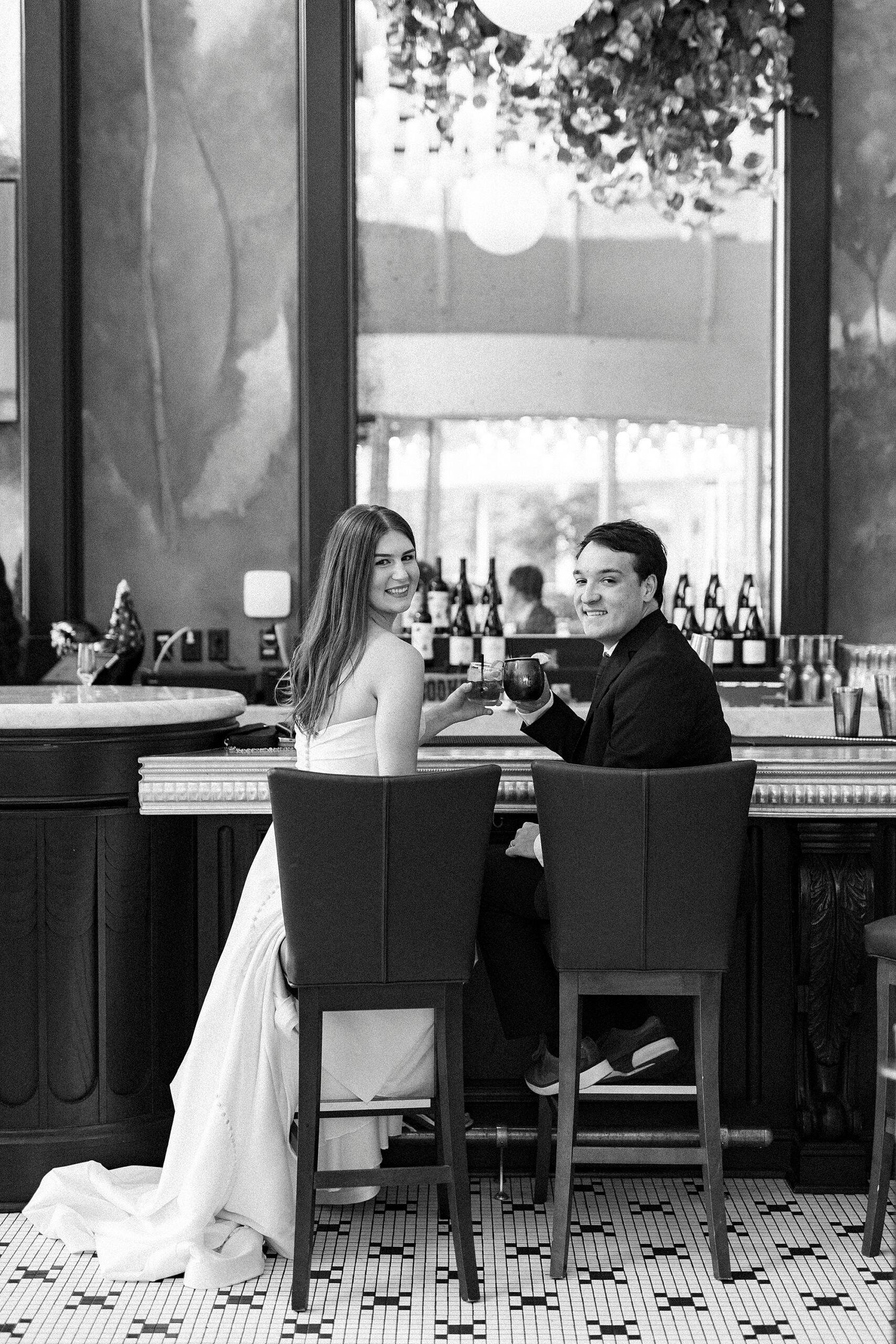 bride and groom sit at bar toasting glasses in French restaurant 