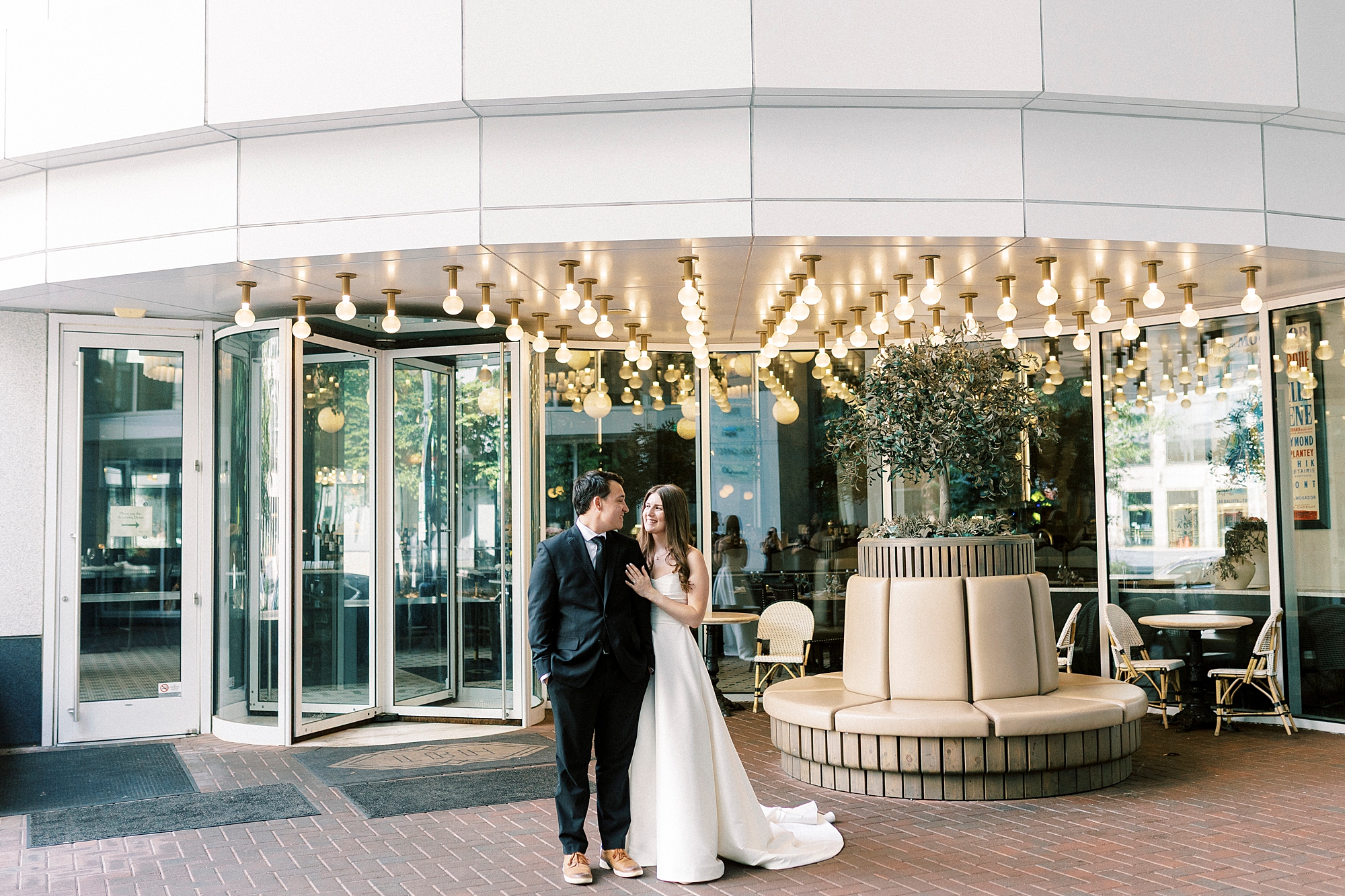 bride and groom stand in front of doors under lights of Charlotte restaurant