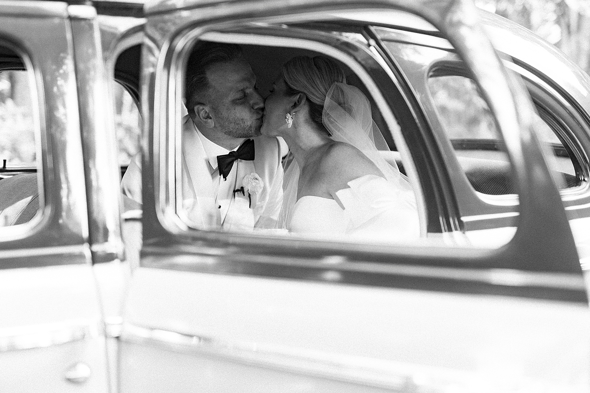 bride and groom kiss in back of car