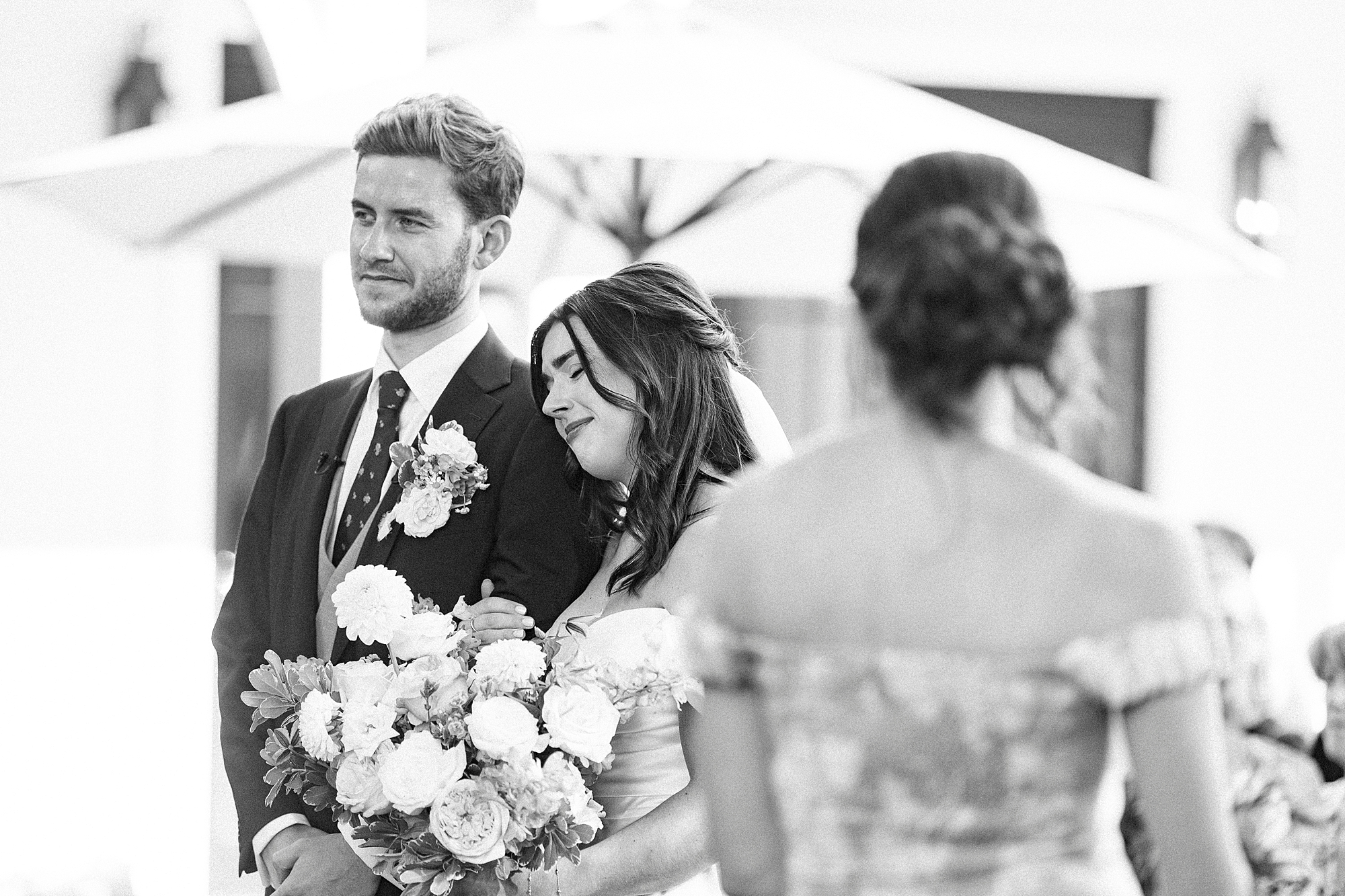 bride lays head on groom's shoulder during wedding ceremony 