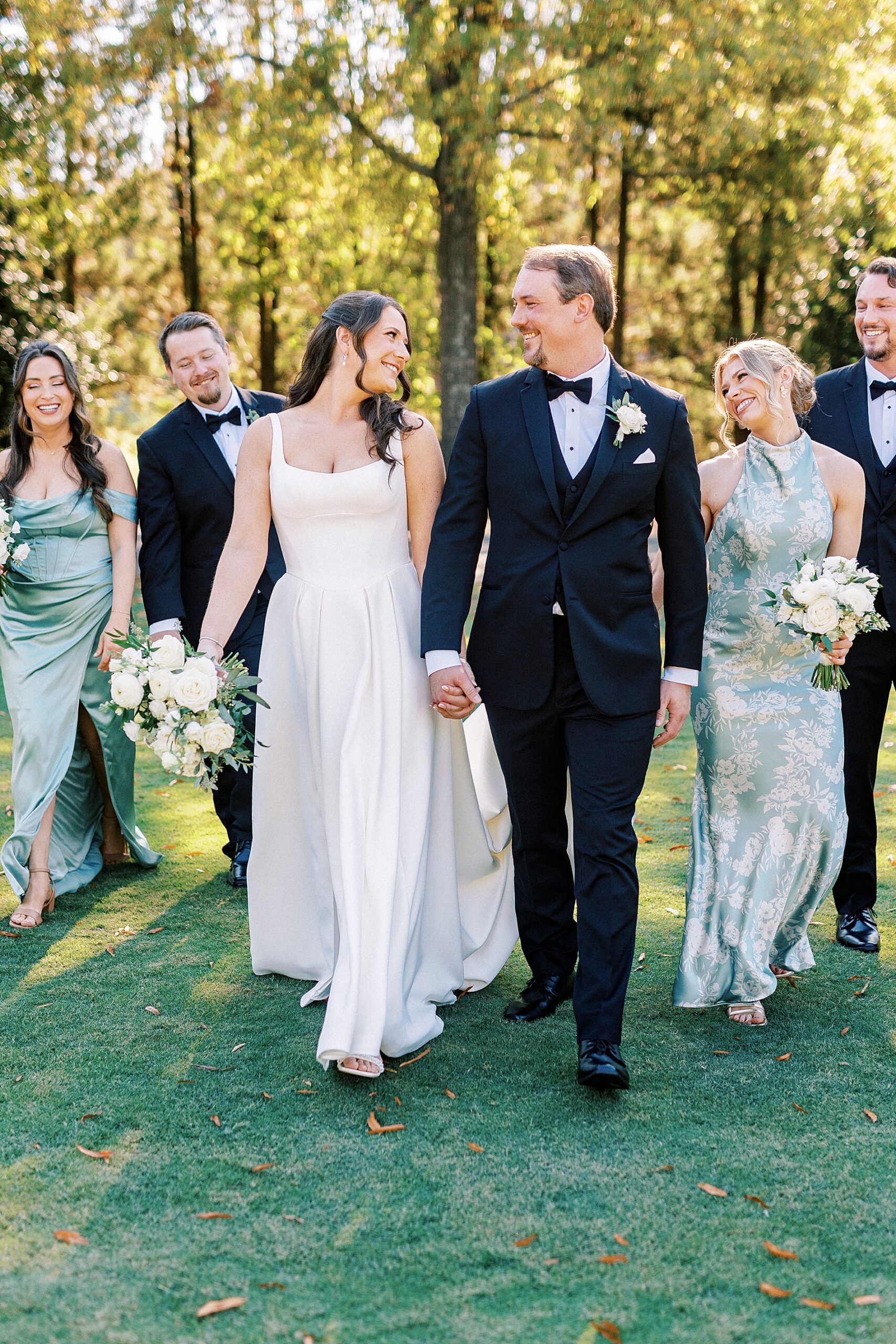 bride and groom walk together holding hands with wedding party walking behind them