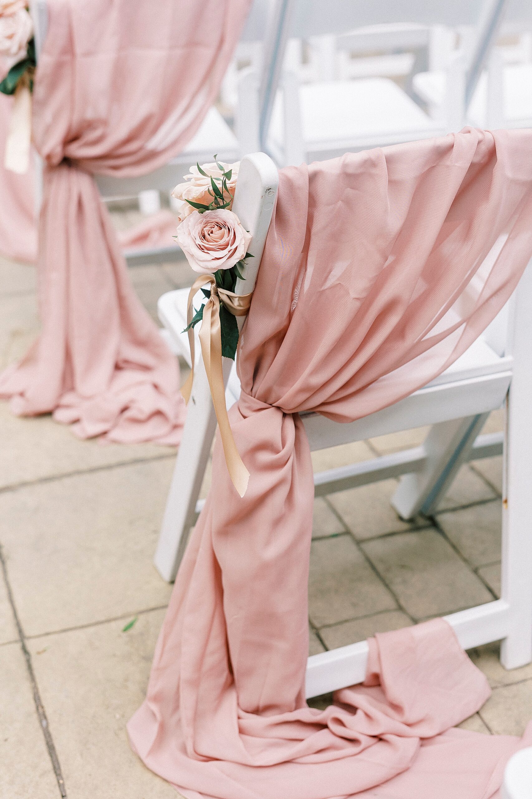 pink fabric and flowers draper over white chairs at wedding ceremony