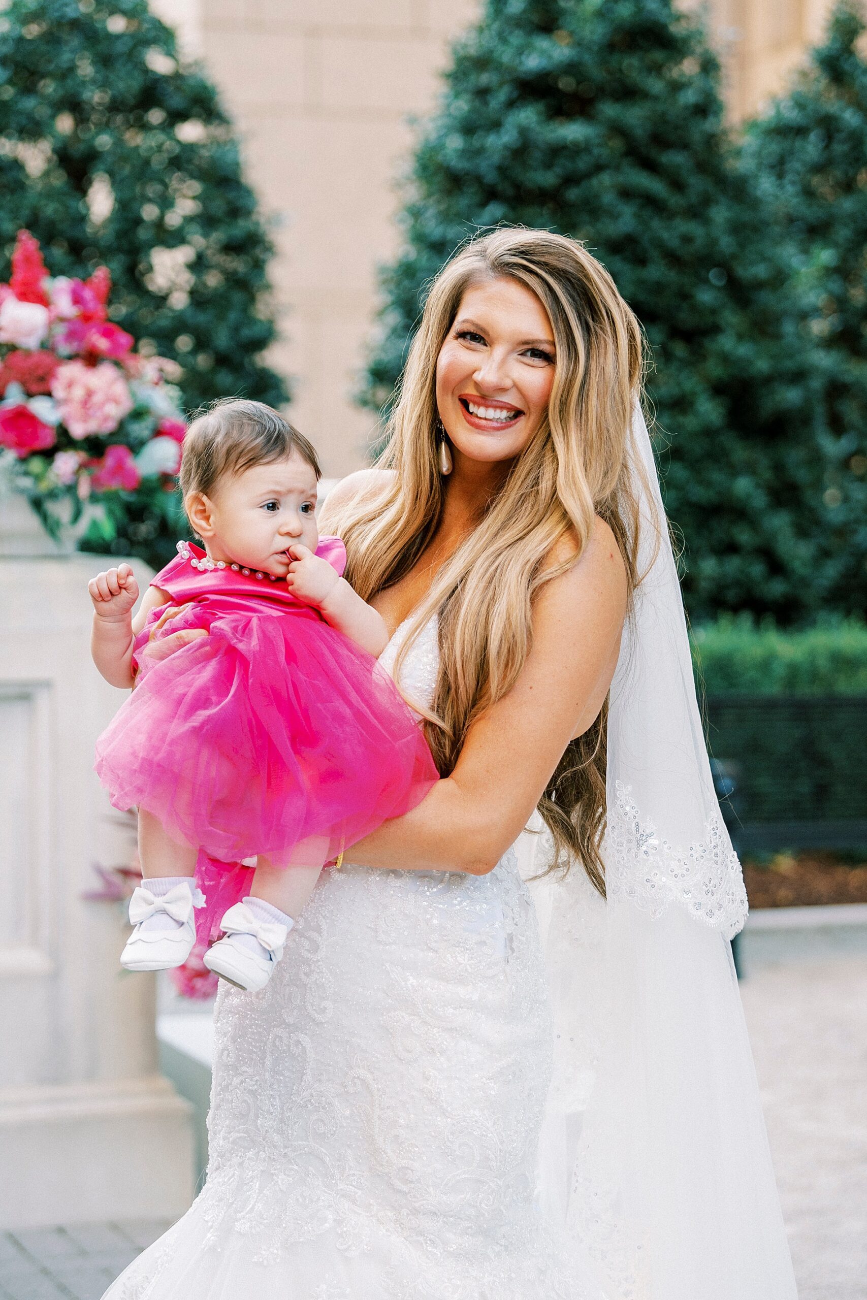bride holding baby in bright pink dress