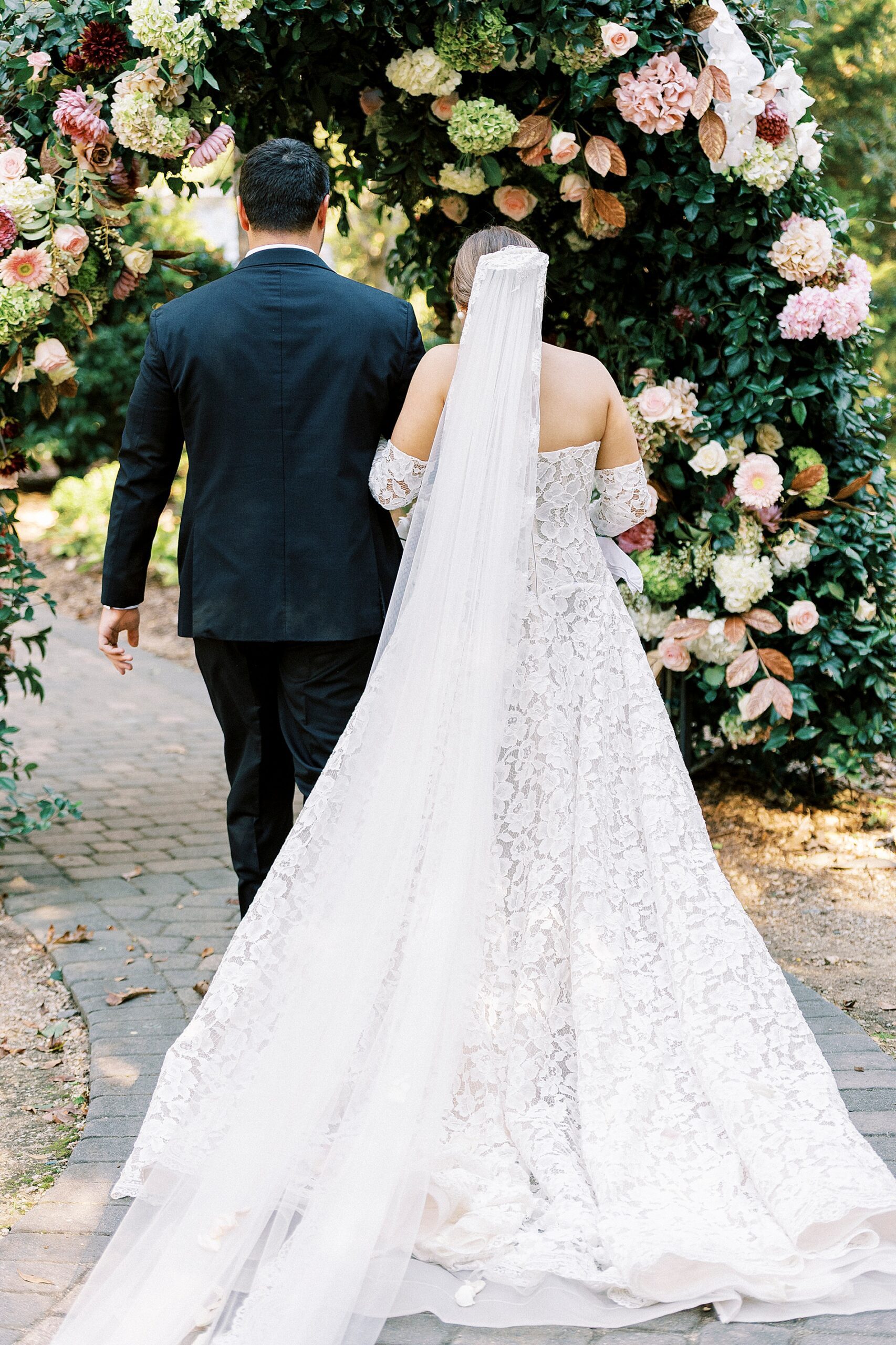 newlyweds walk under floral arch 