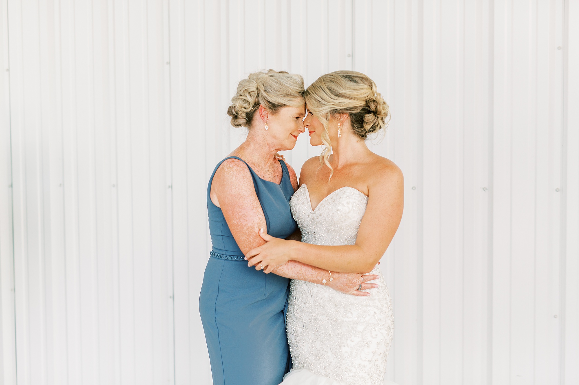 bride and mom stand nose to nose hugging during wedding prep