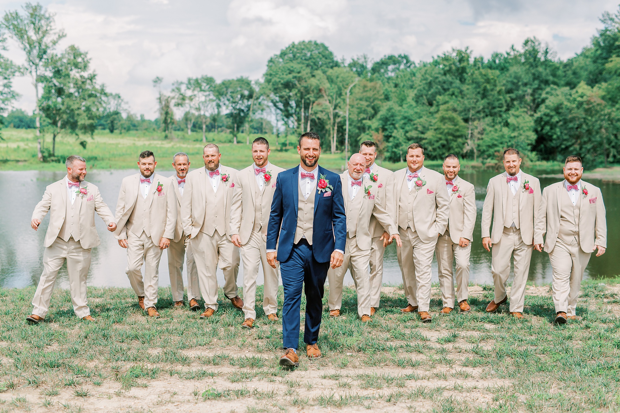 groom in navy suit walks with groomsmen in tan suits behind him