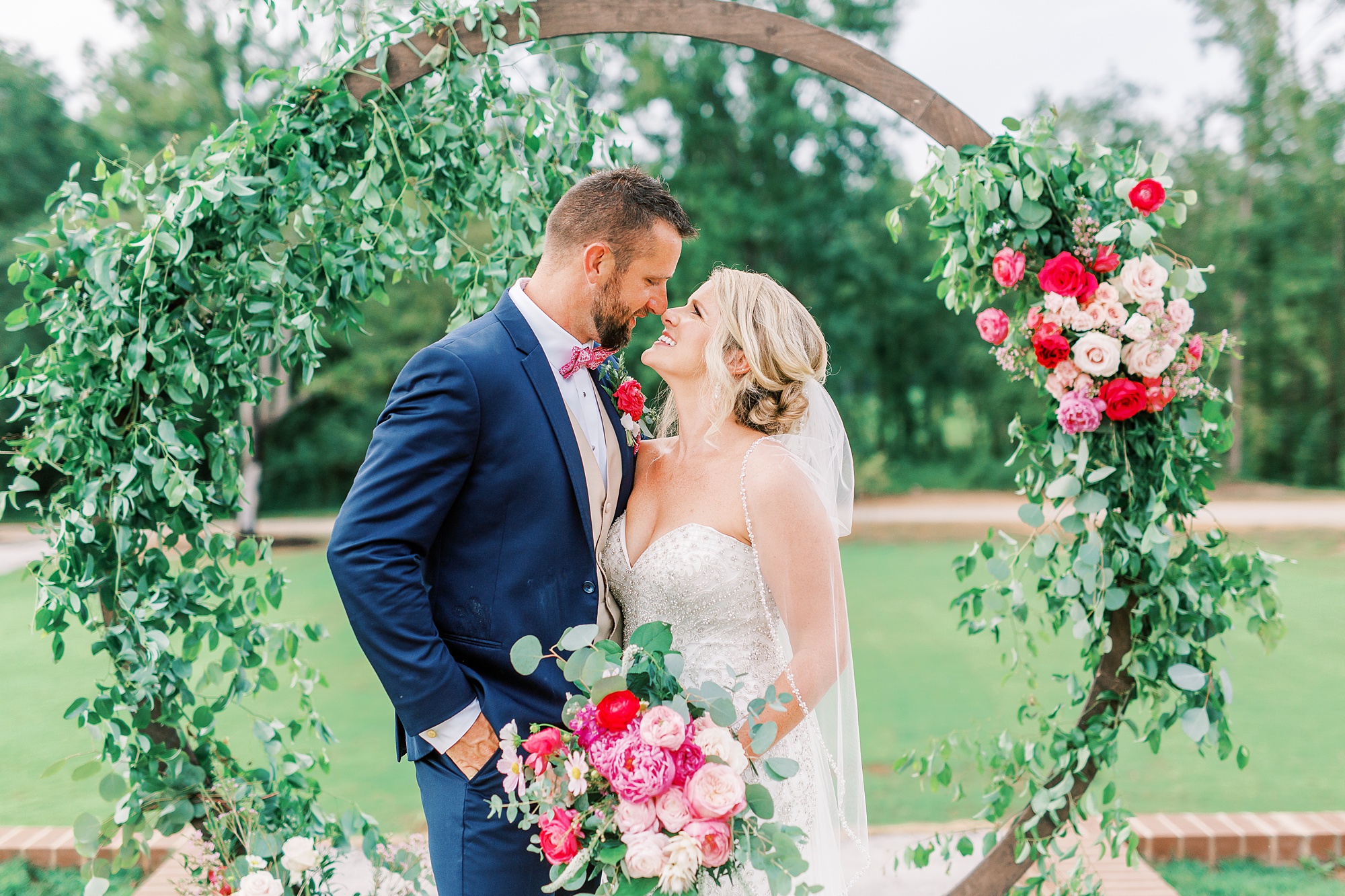 bride and groom look at each other in front of floral arbor