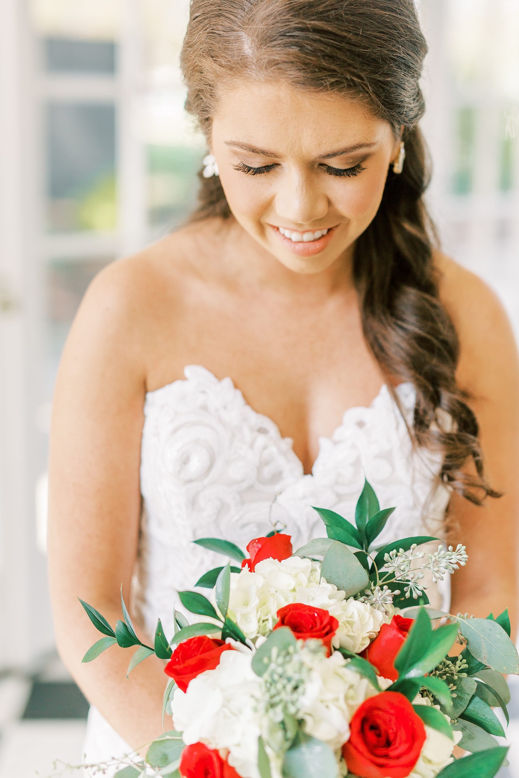 bride looks down at bouquet with red flowers