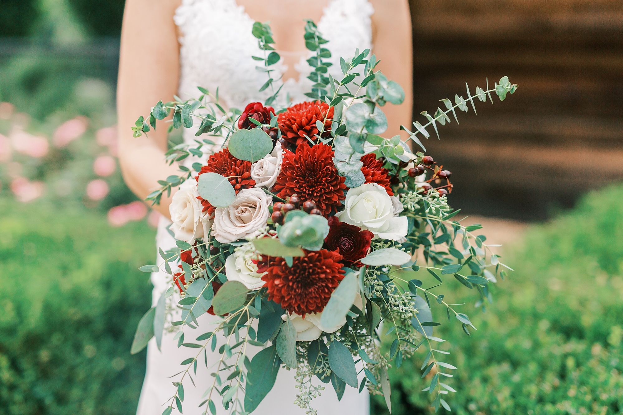 bride holds summer bouquet with red flowers and white roses