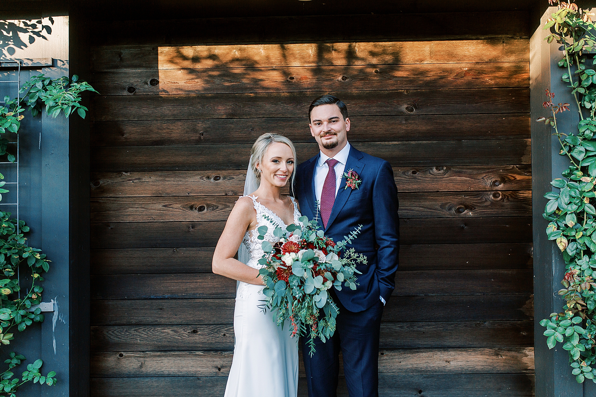 bride and groom pose by wooden wall