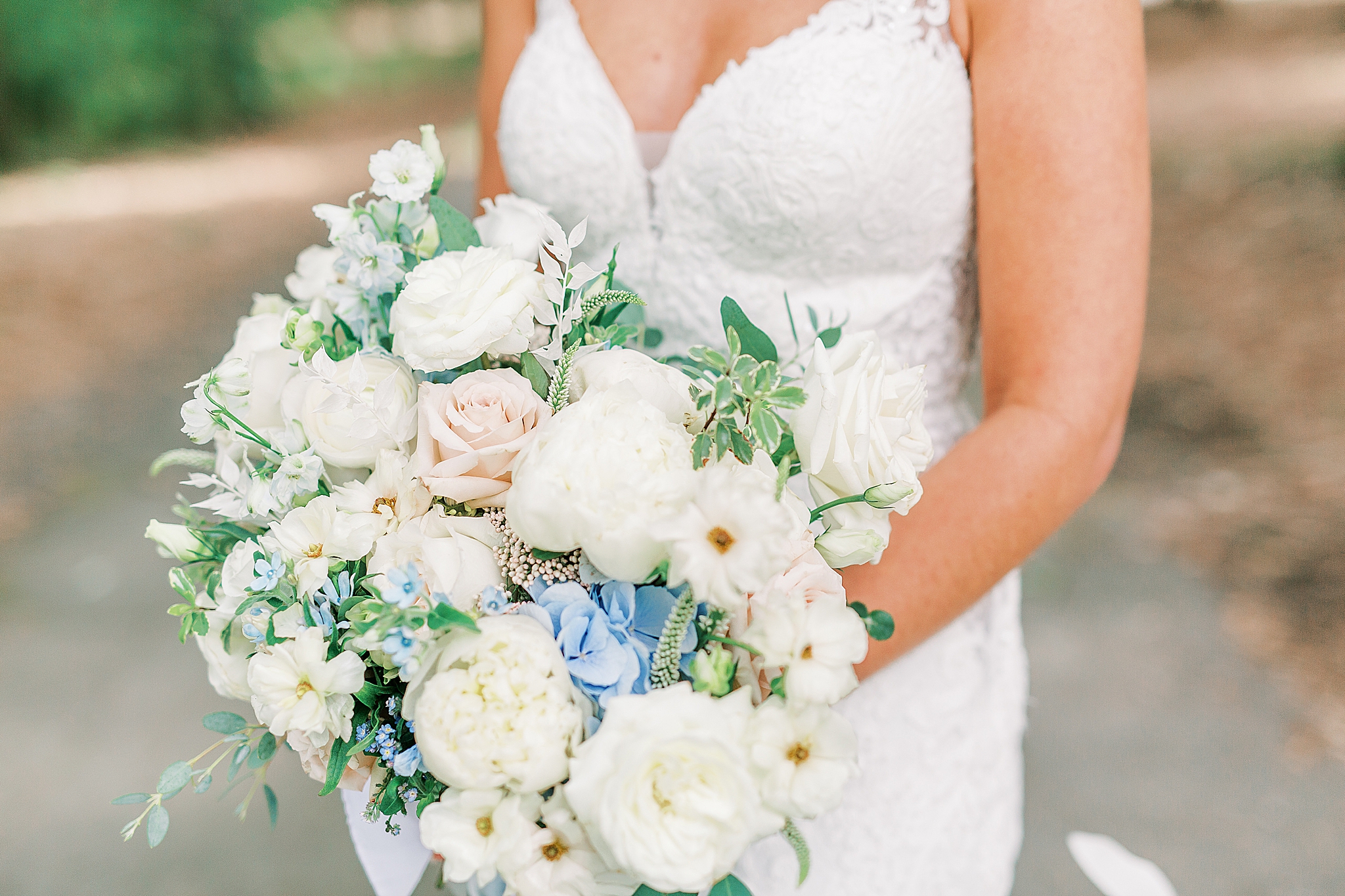 bride holds bouquet of white flowers with pink and blue accents
