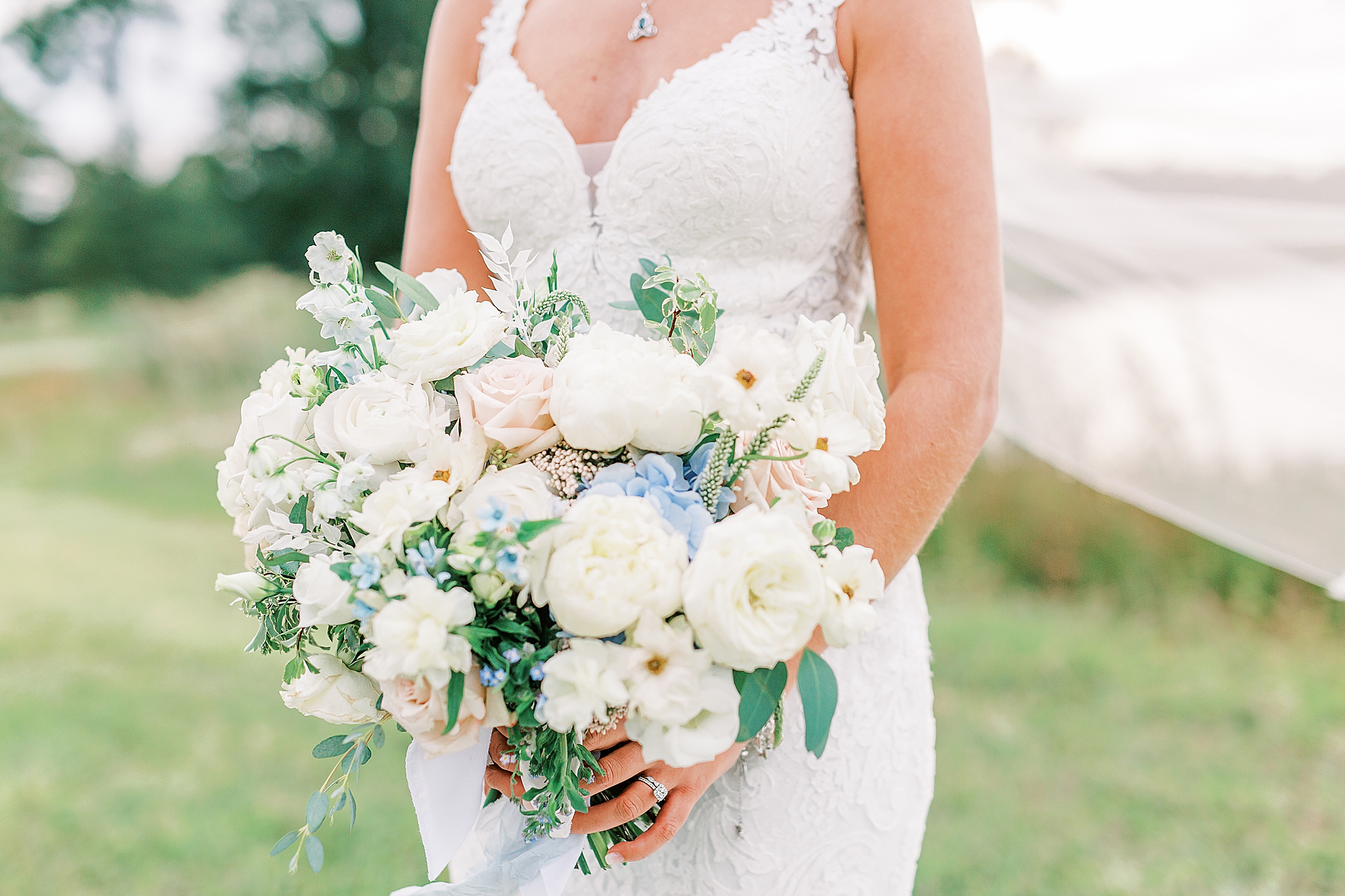 bride holds bouquet with white, blue, and pastel pink flowers