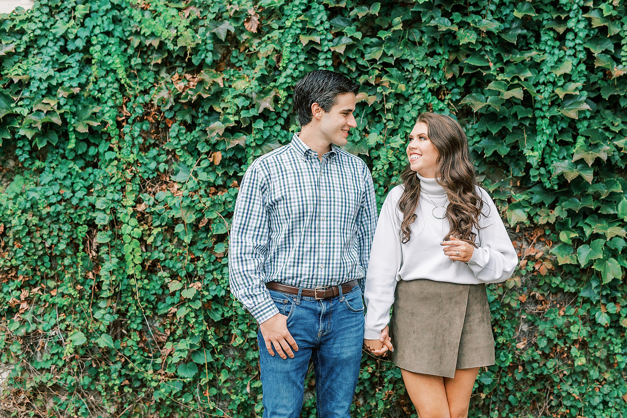 engaged couple poses by ivy covered wall