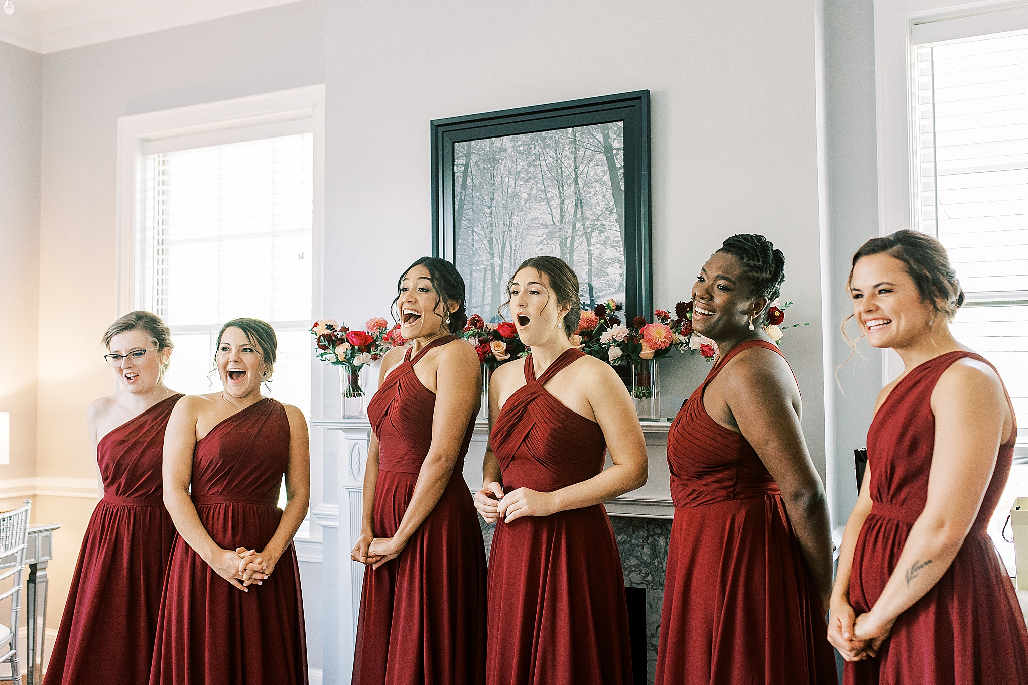 bridesmaids in red gowns react to seeing bride for the first time