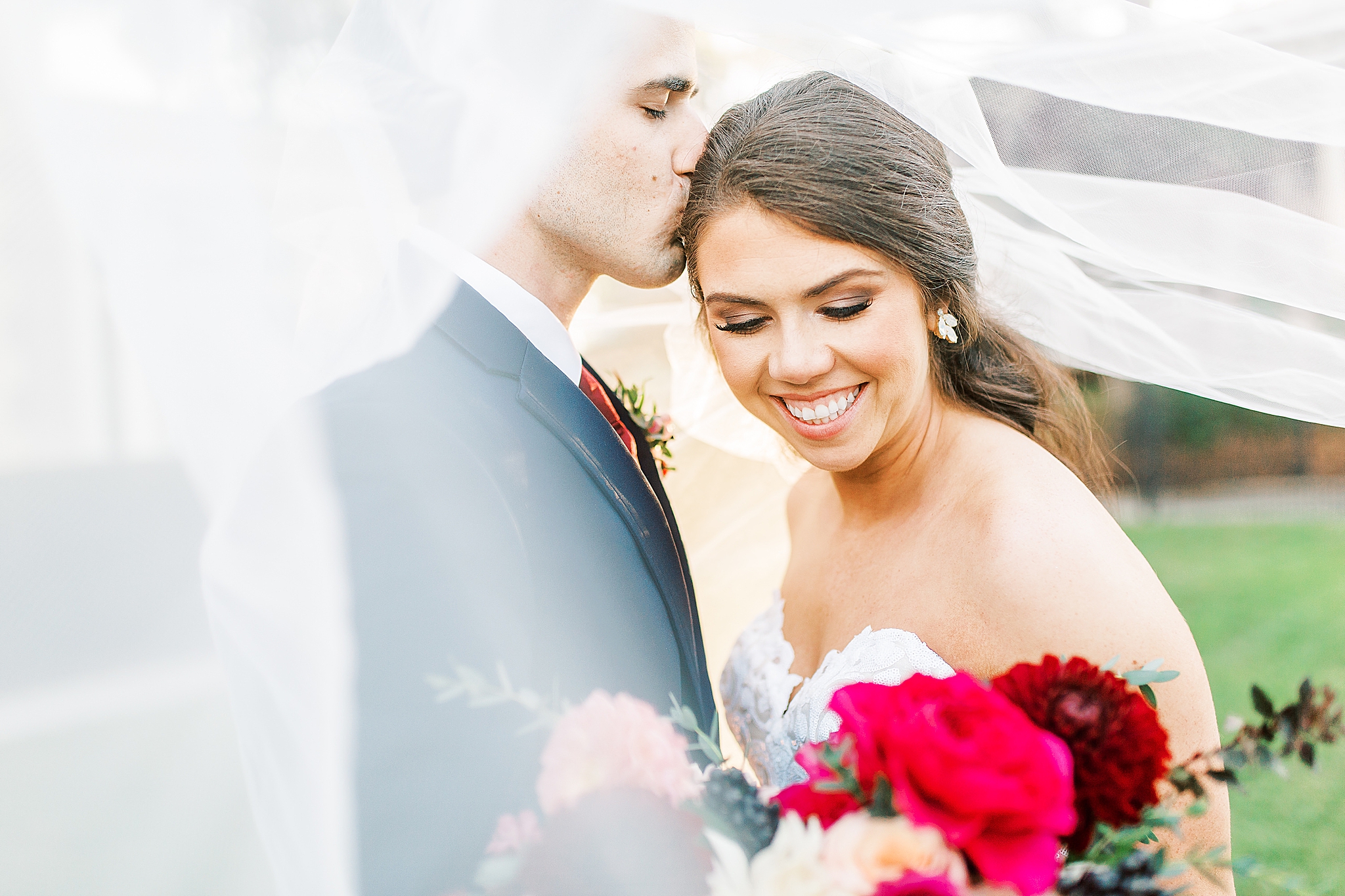 groom kisses bride as veil floats around them