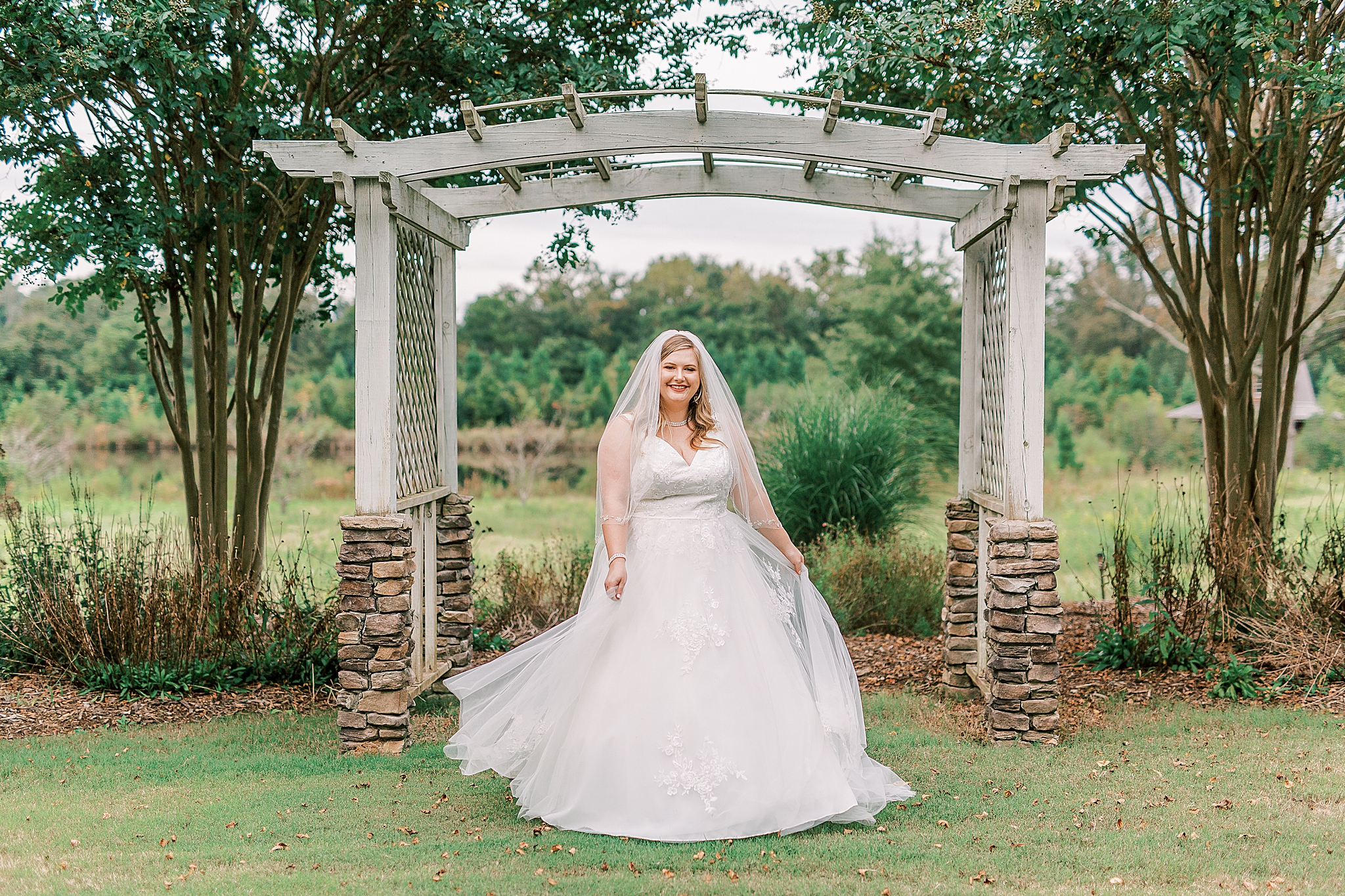 bride poses in front of wooden arbor