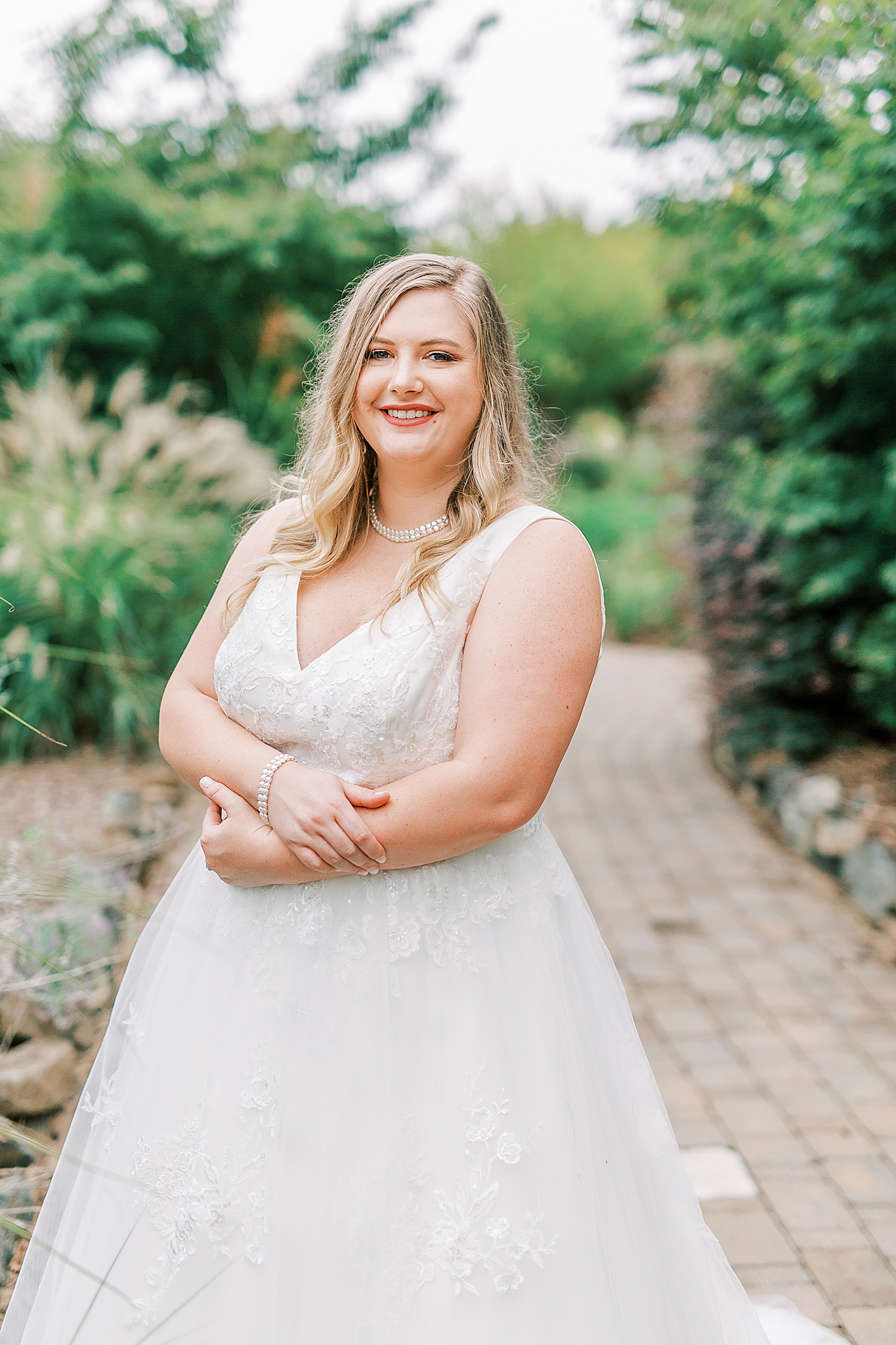 bride stands with arms crossed on brick walkway at The Arbors
