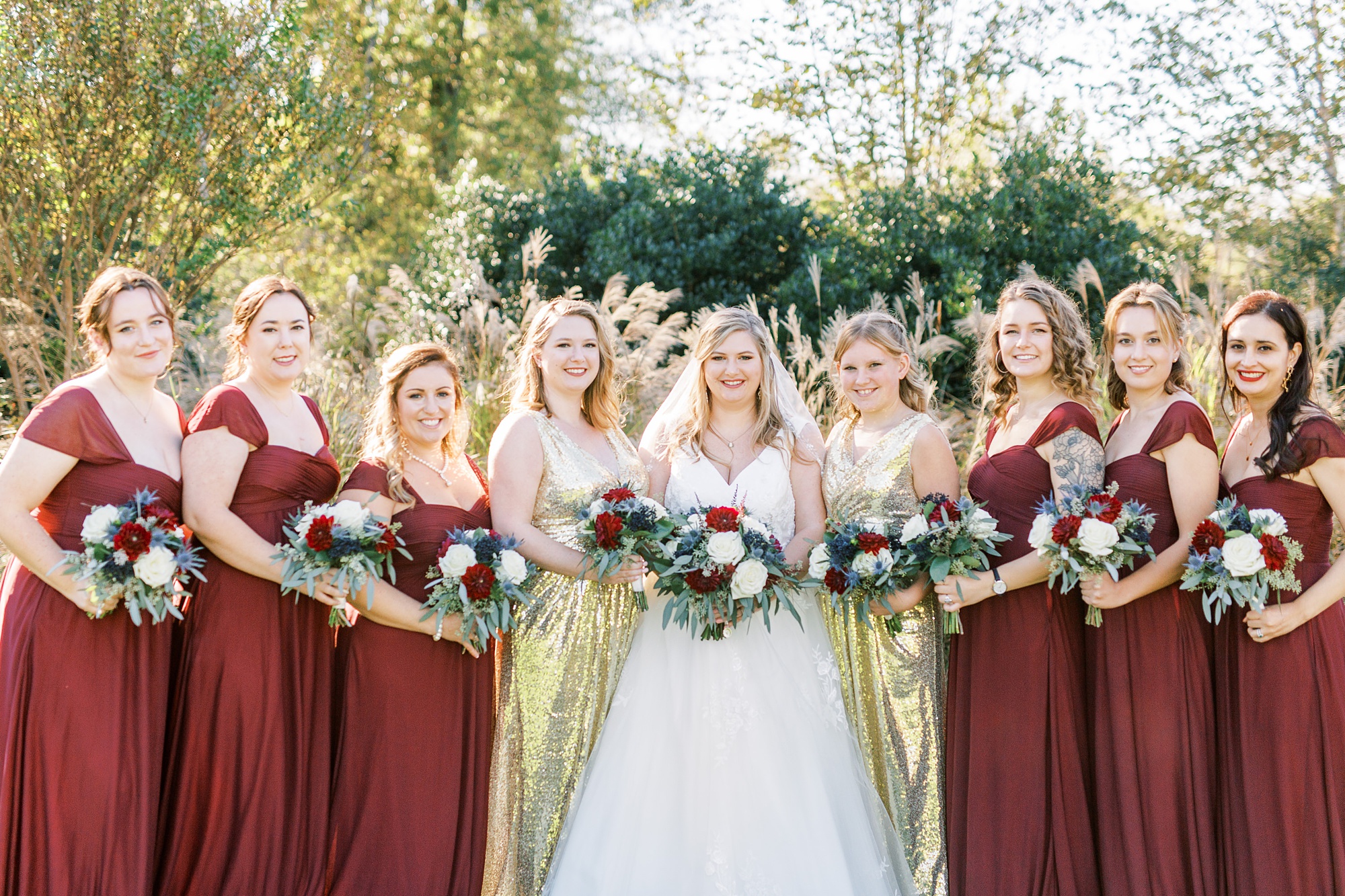 bridesmaids in red and gold pose with bride
