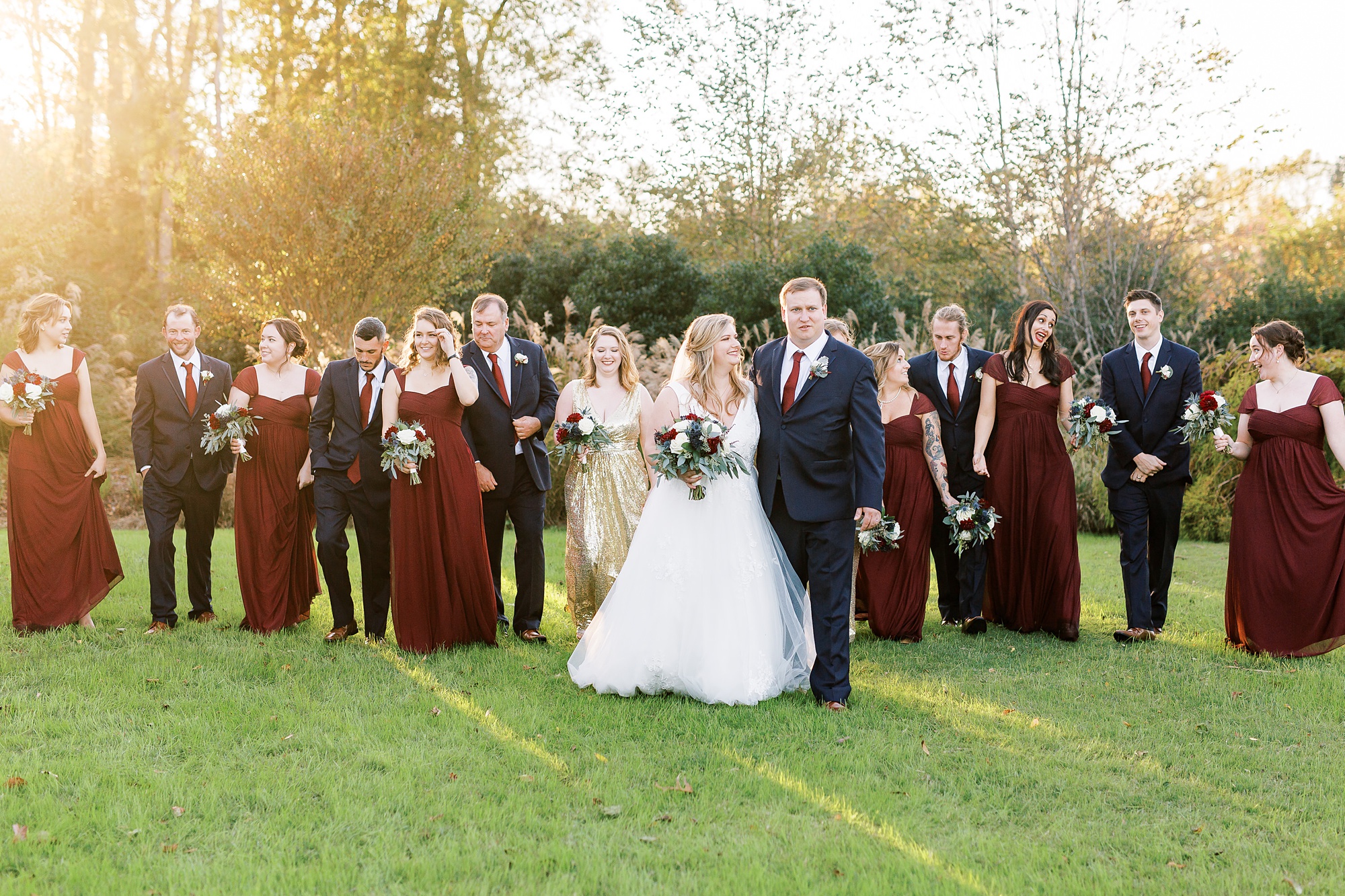 fall bridal party in navy and cranberry walks with bride and groom