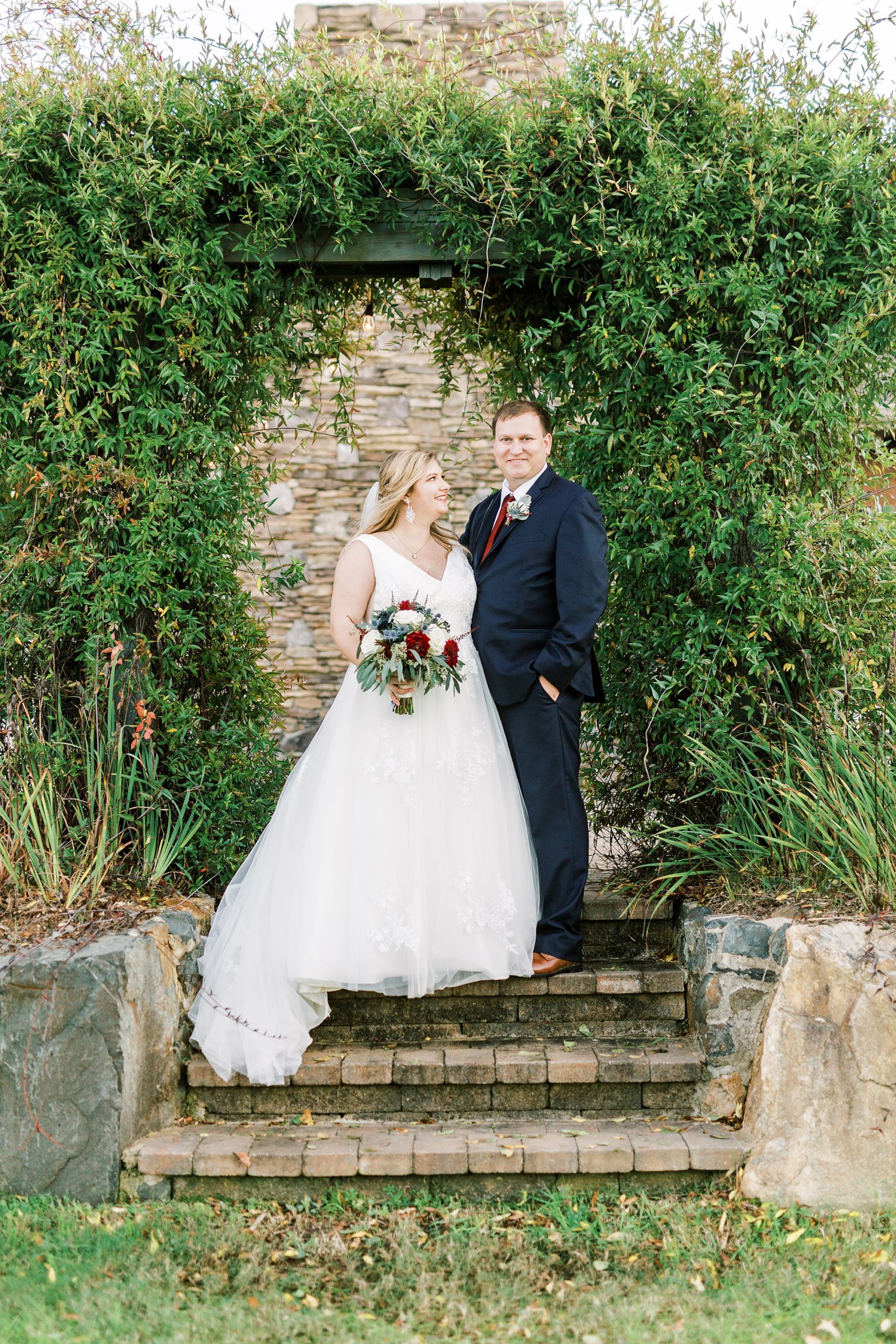 bride and groom pose by ivy covered wall at the Arbors Events