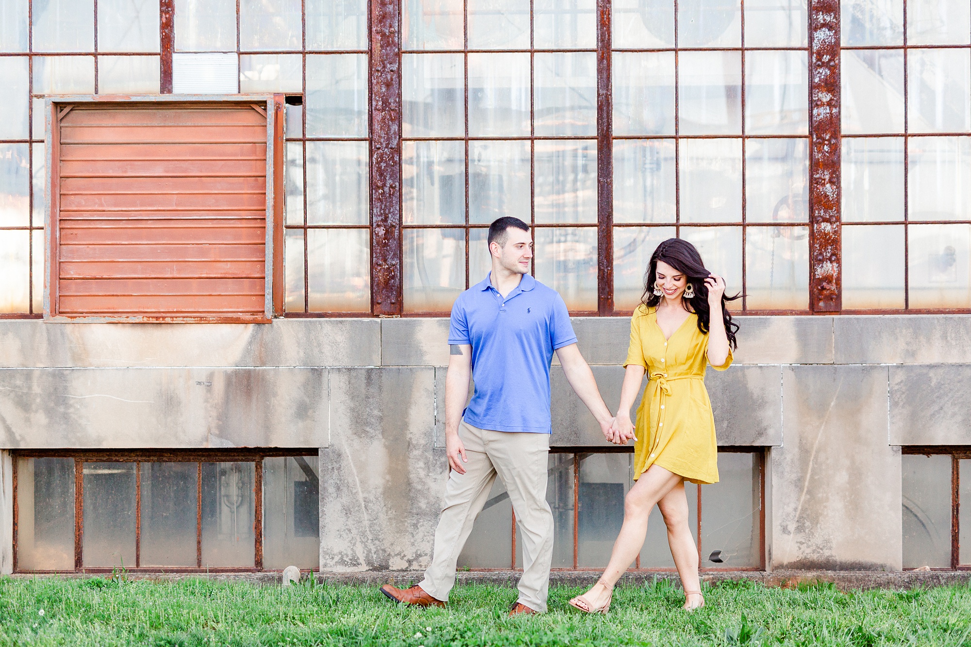 engaged couple walks in front of industrial warehouse