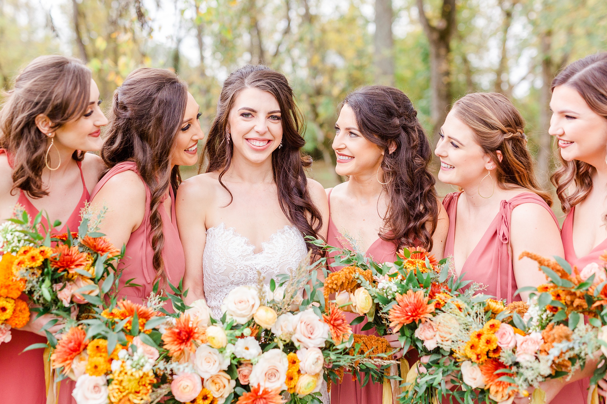 bridesmaids holding bouquets of ivory and burnt orange smile at bride