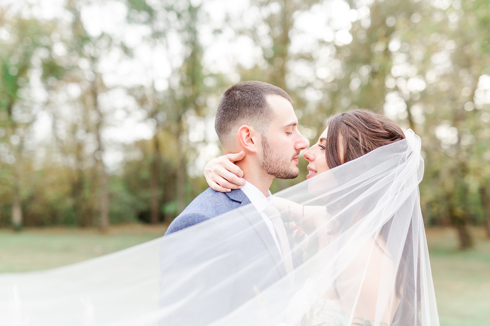 bride and groom kiss while veil wraps around them