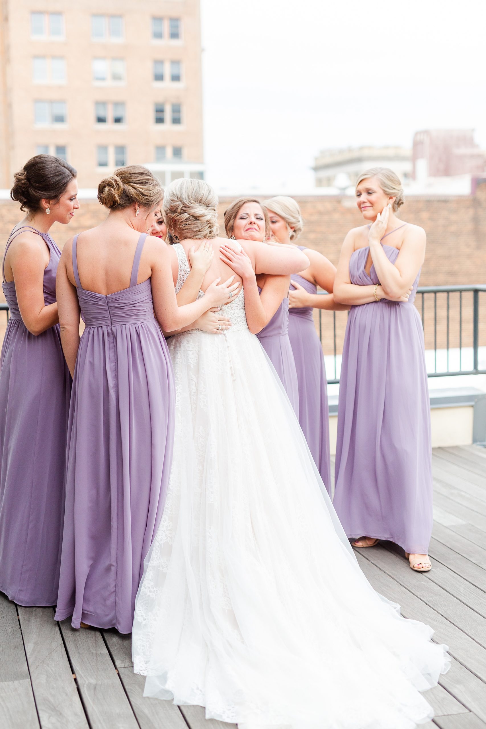 bride hugs bridesmaids in purple dresses during first look