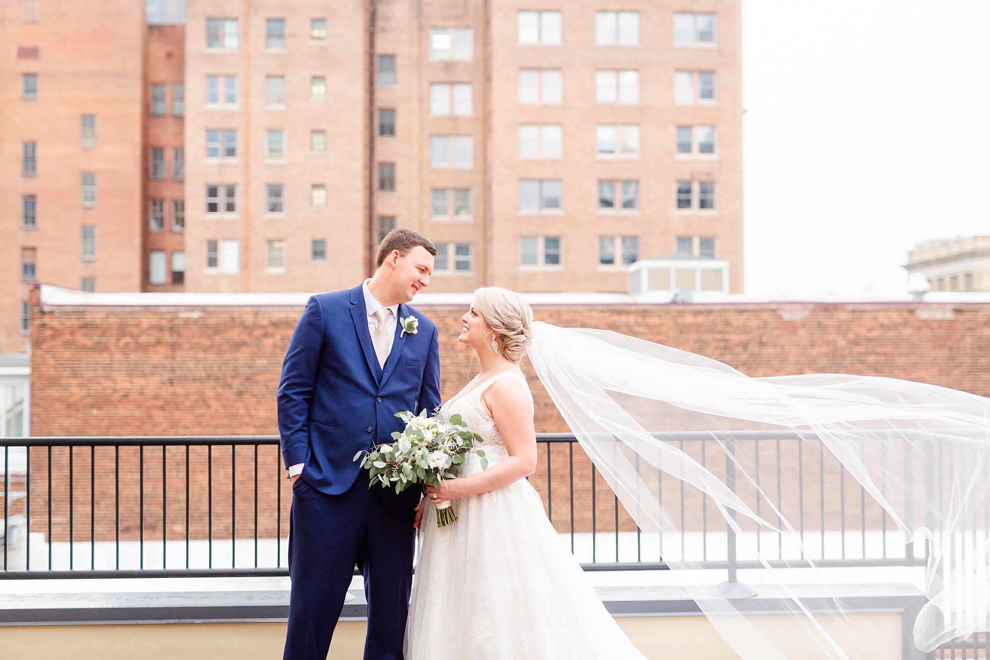 bride and groom pose on rooftop with veil floating