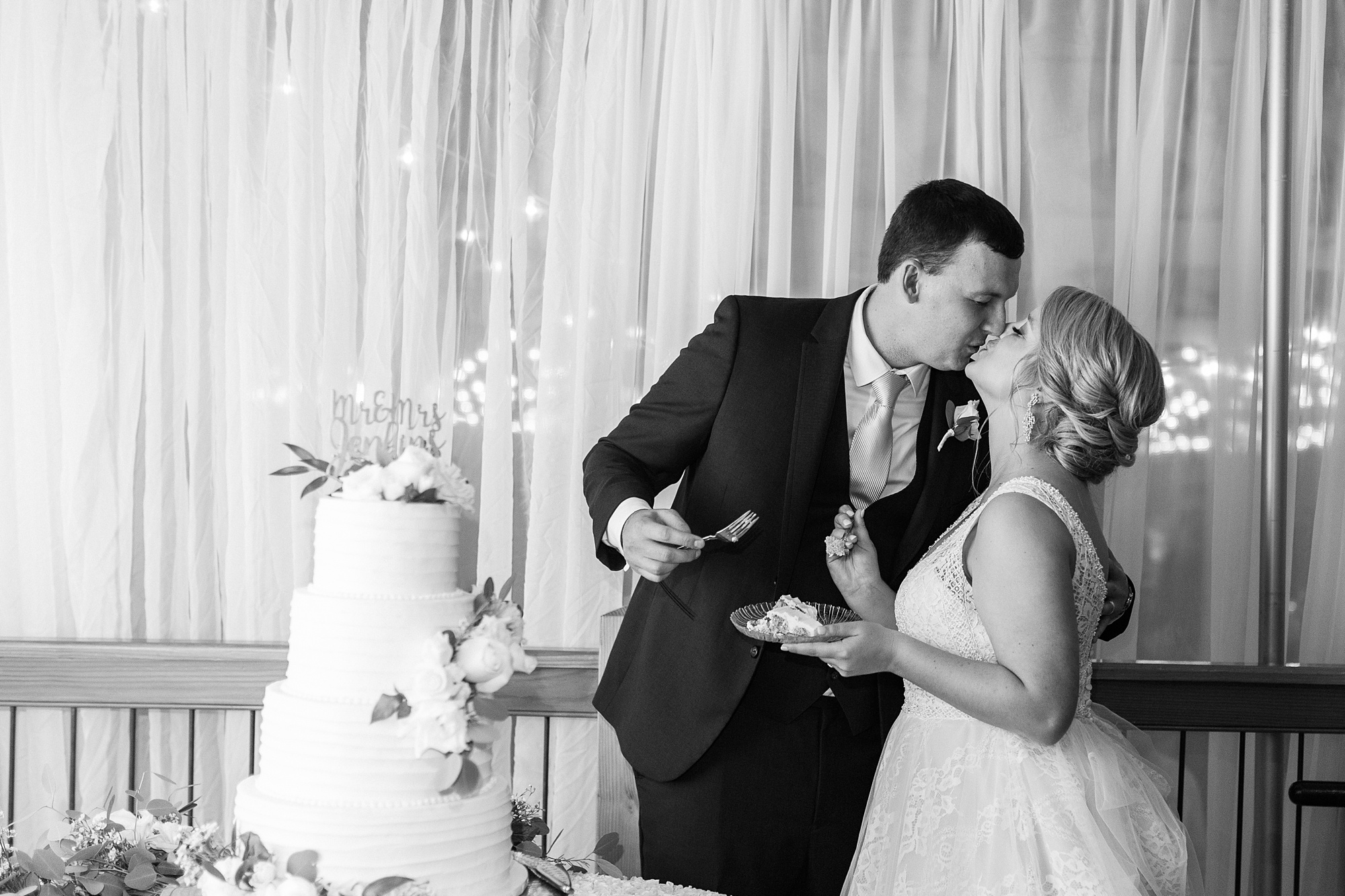 newlyweds kiss after cutting wedding cake at Raleigh NC wedding reception