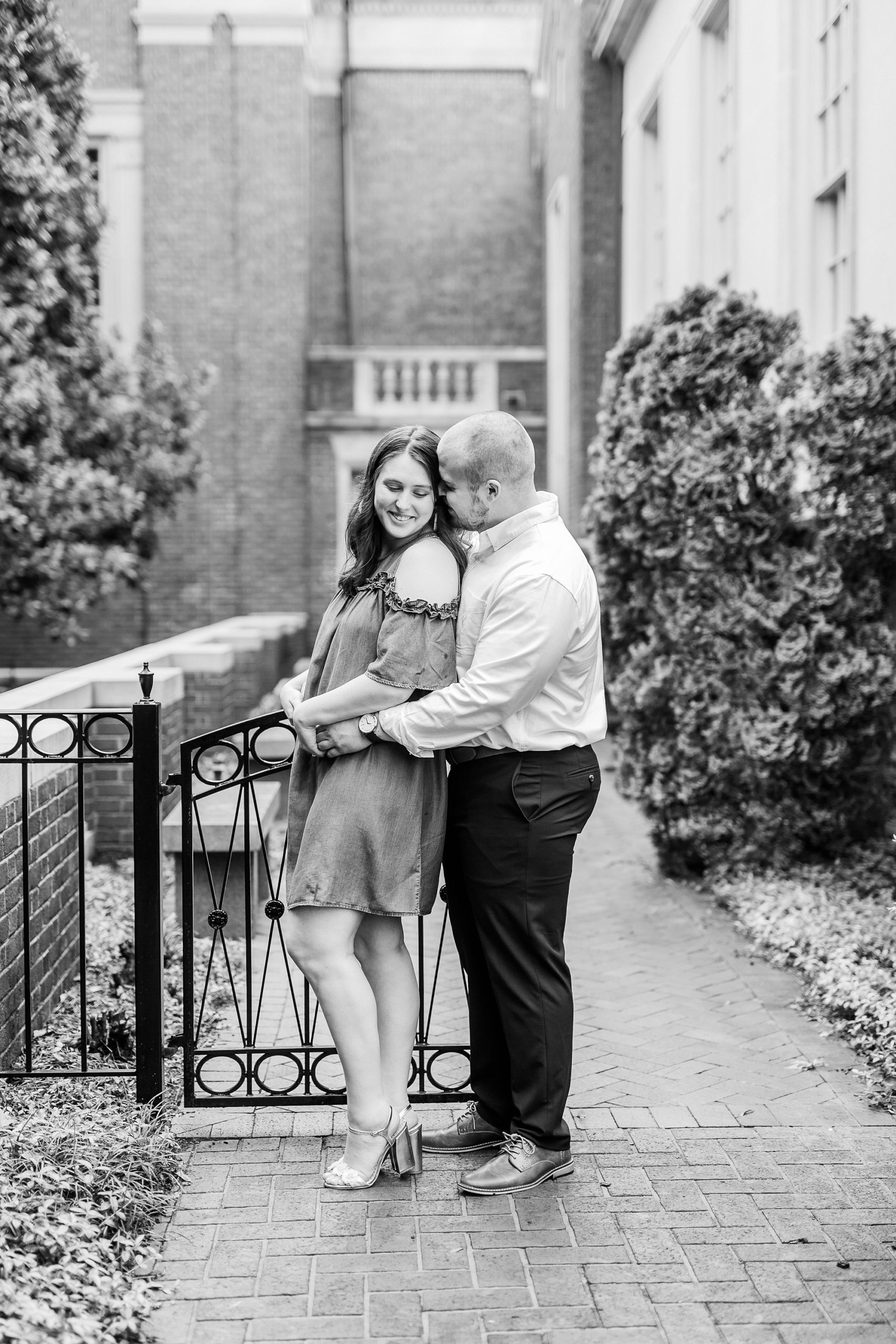 groom hugs bride from behind during Downtown Davidson engagement portraits