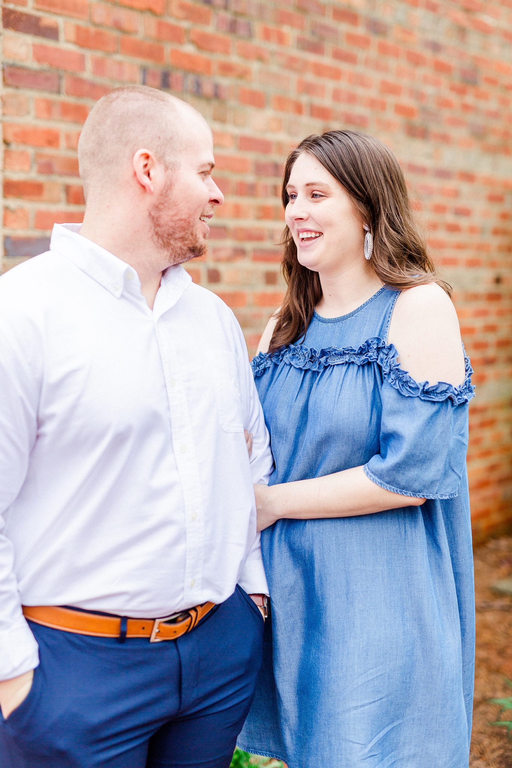 engaged couple laughs next to brick wall in Downtown Davidson