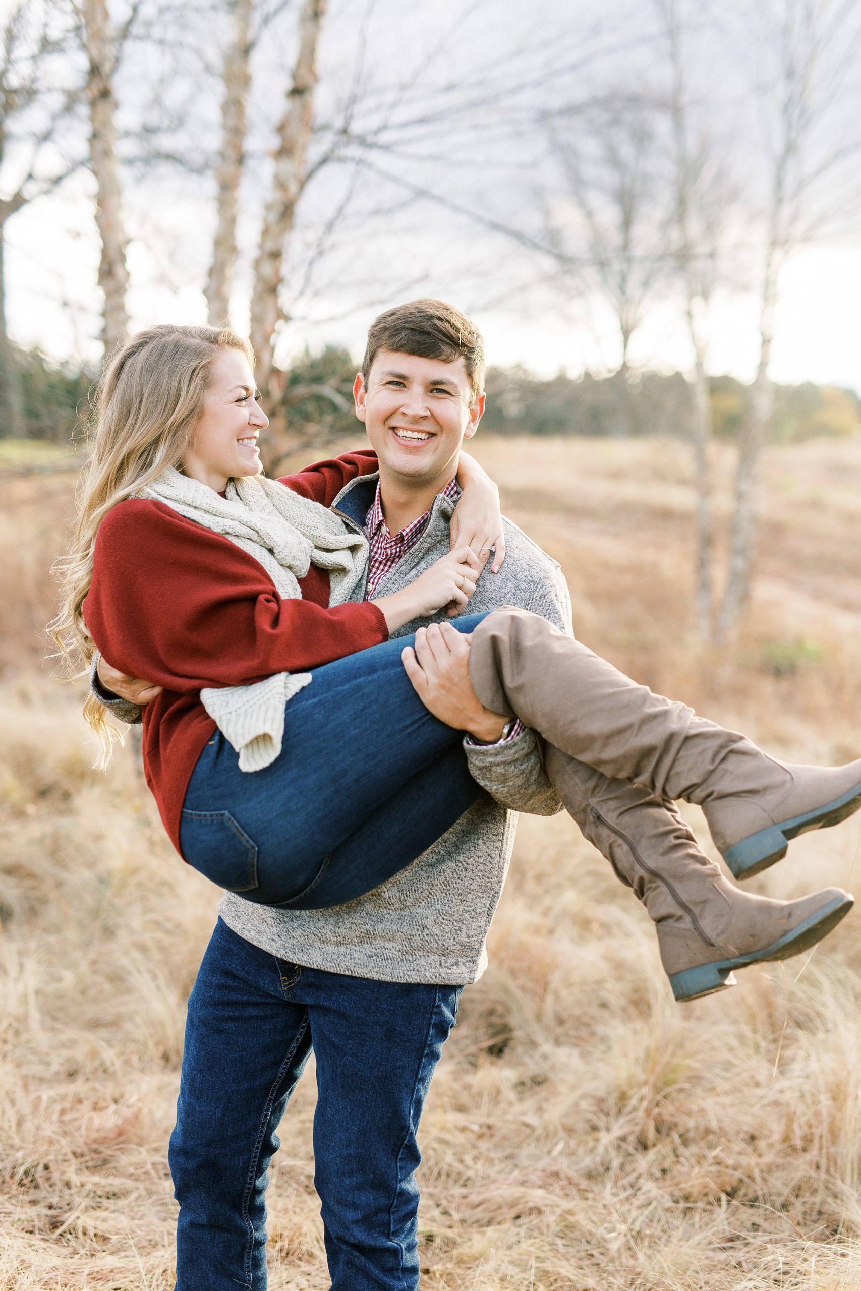 groom lifts bride-to-be in field during fall engagement photos
