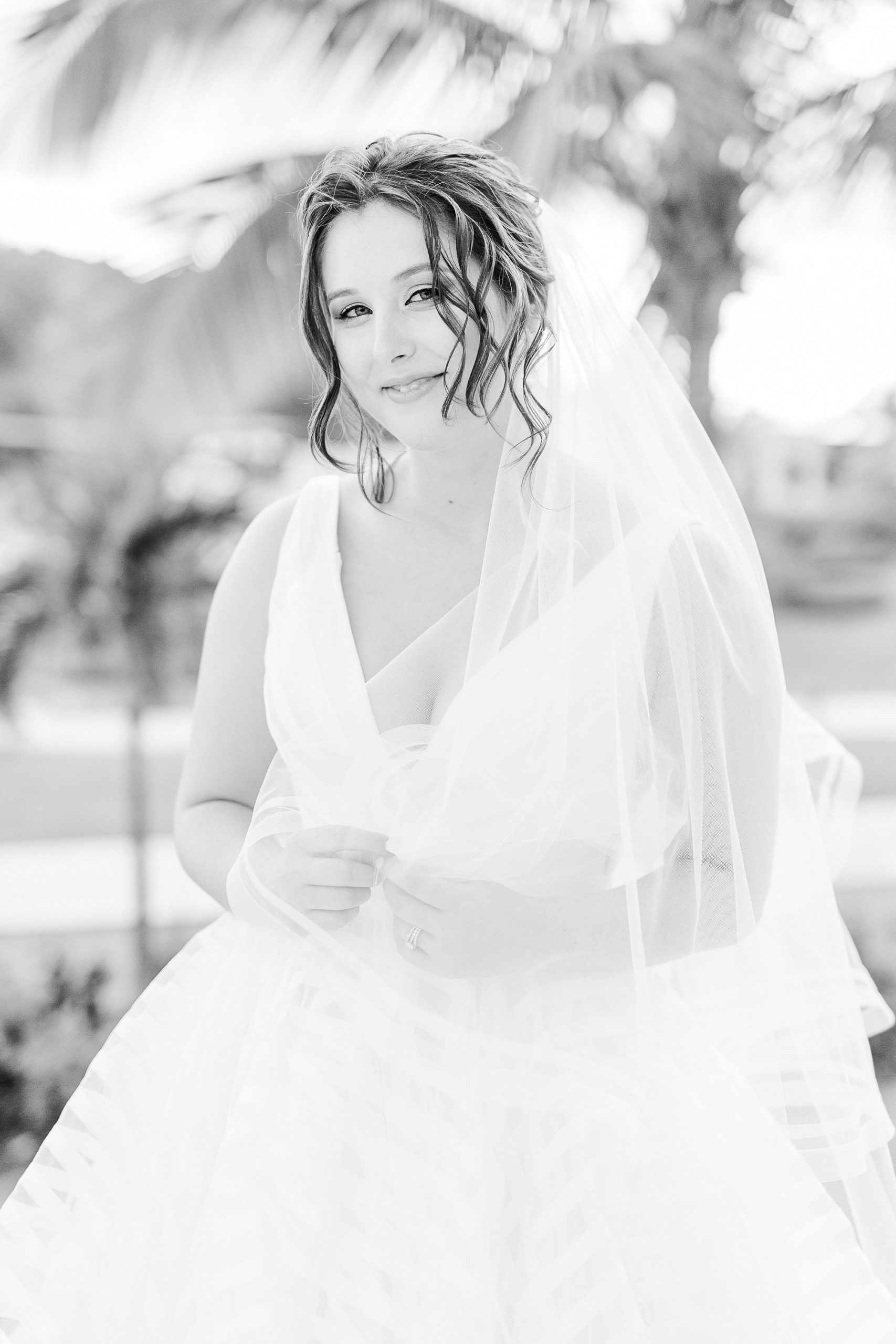 bride holds veil in hands during portraits on beach