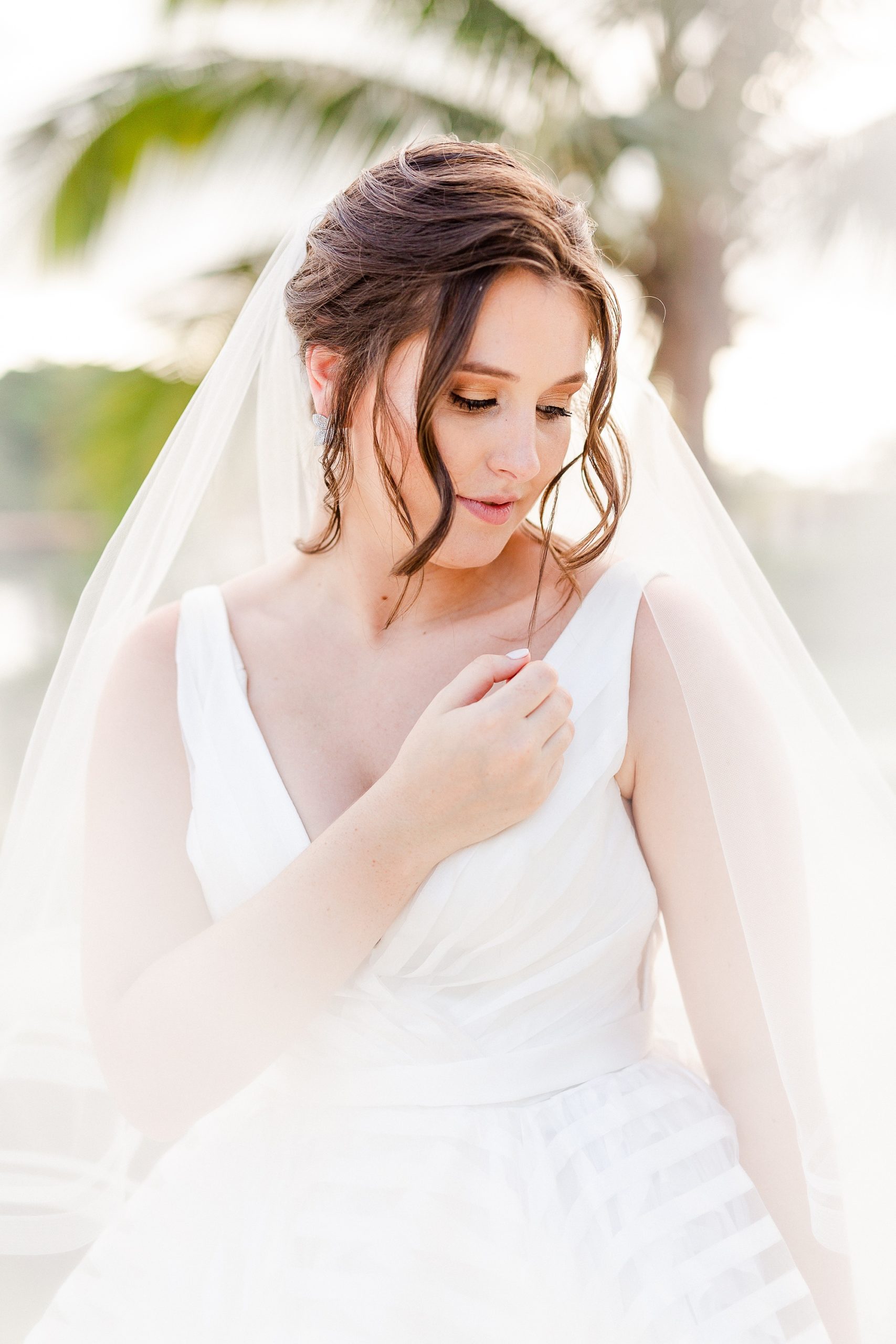 bride poses with veil around arms on beach