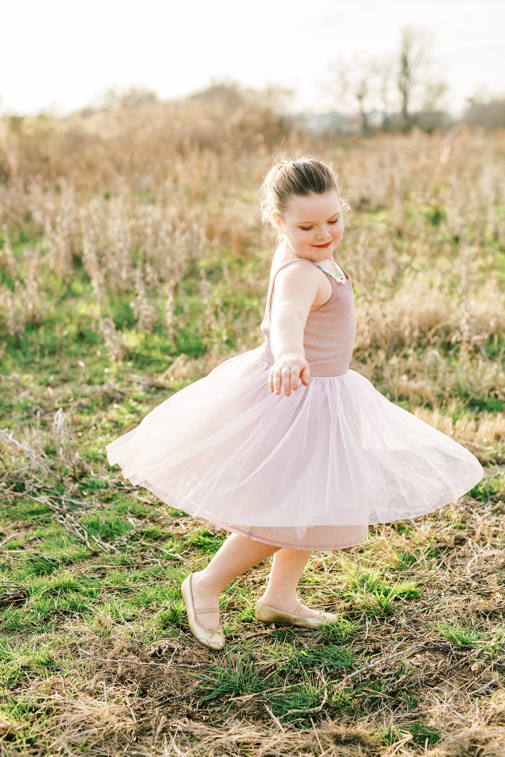 girl twirls in field wearing pink dress