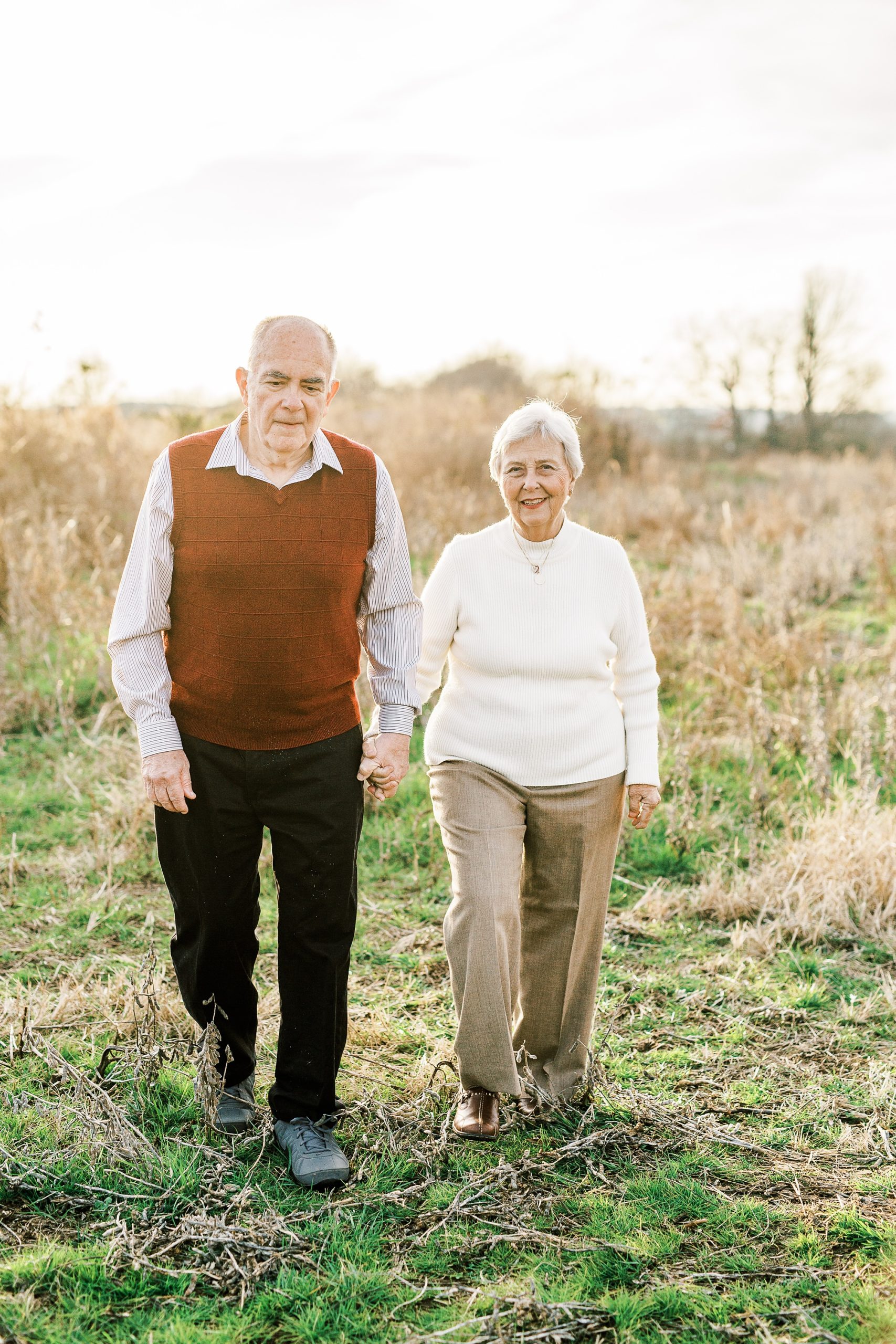 married couple walks through field during 50th anniversary photos