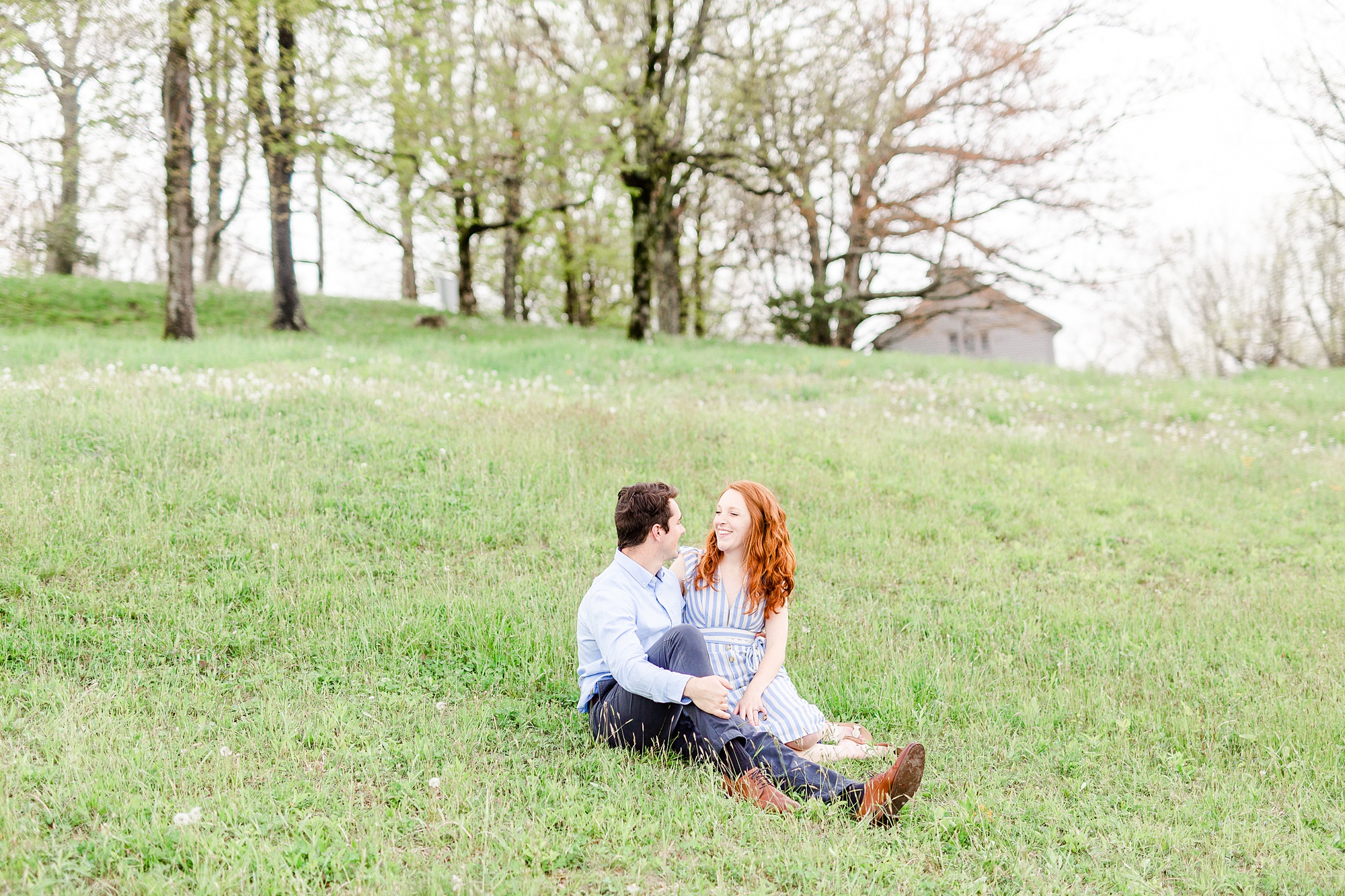 engaged couple sits in grass at Moses Cone Manor