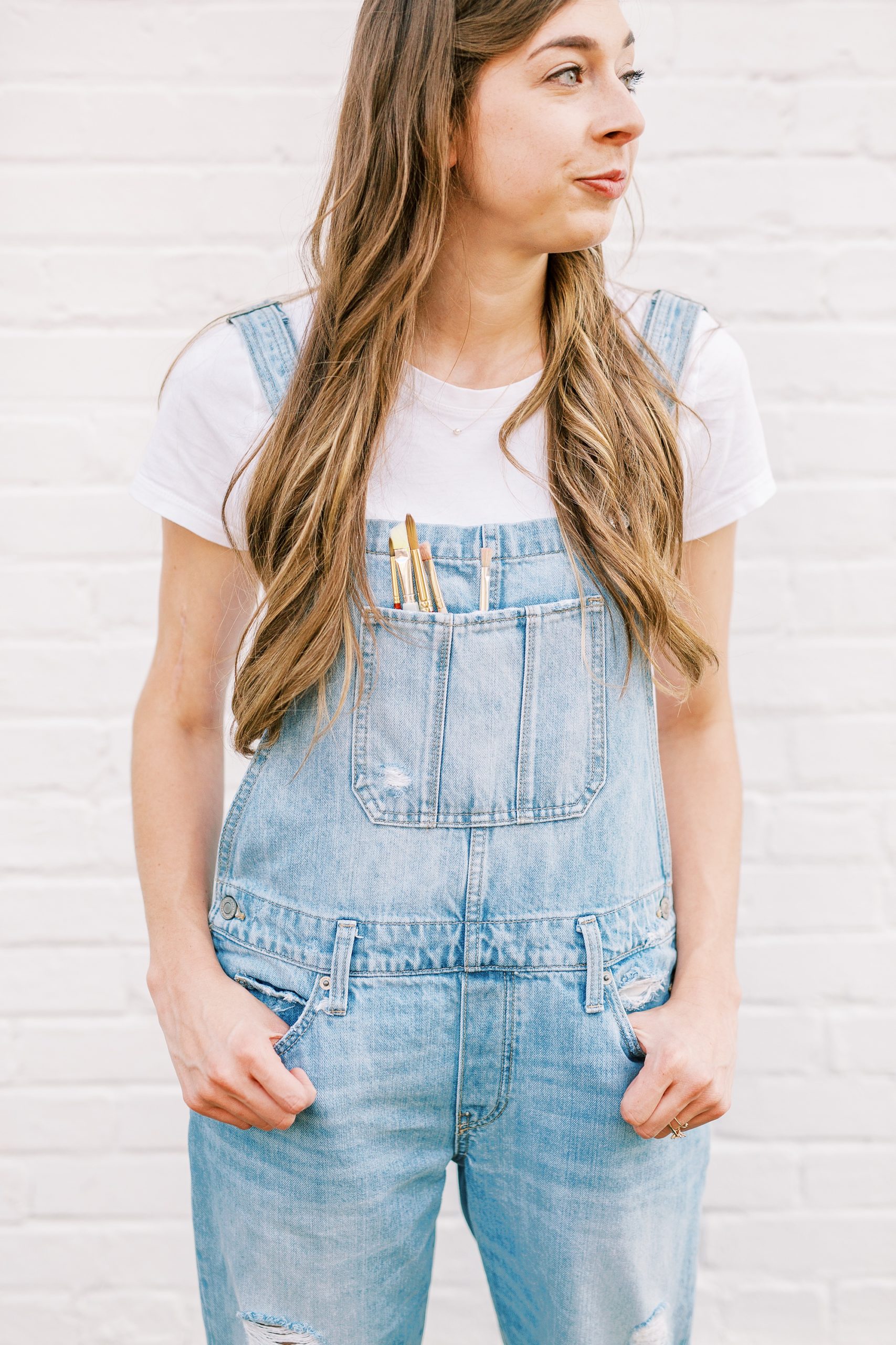 NC artist in overalls in front of white wall during branding portraits