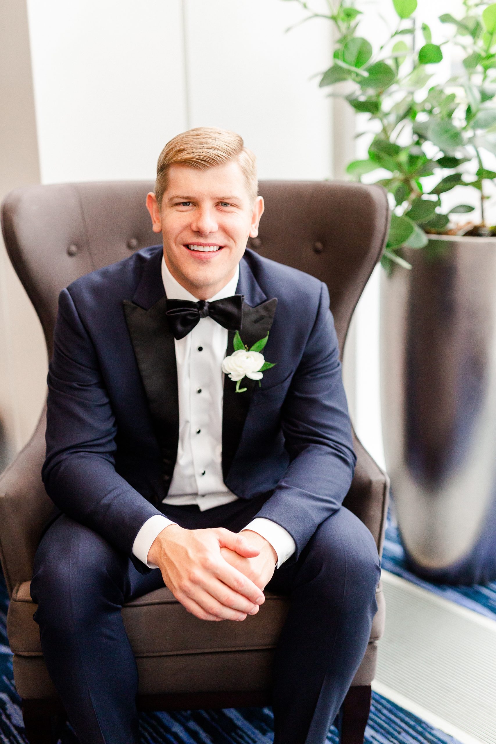 groom in navy tux poses in chair at Kimpton Hotel