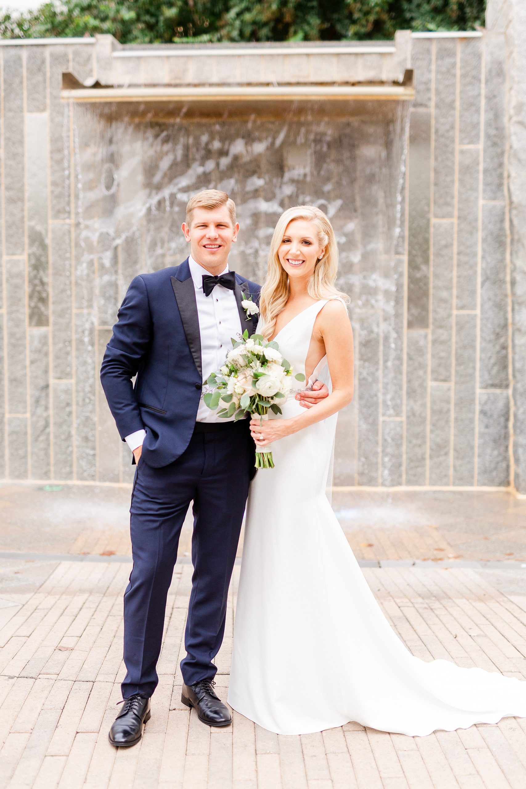bride and groom pose by waterfall at Romare Bearden Park