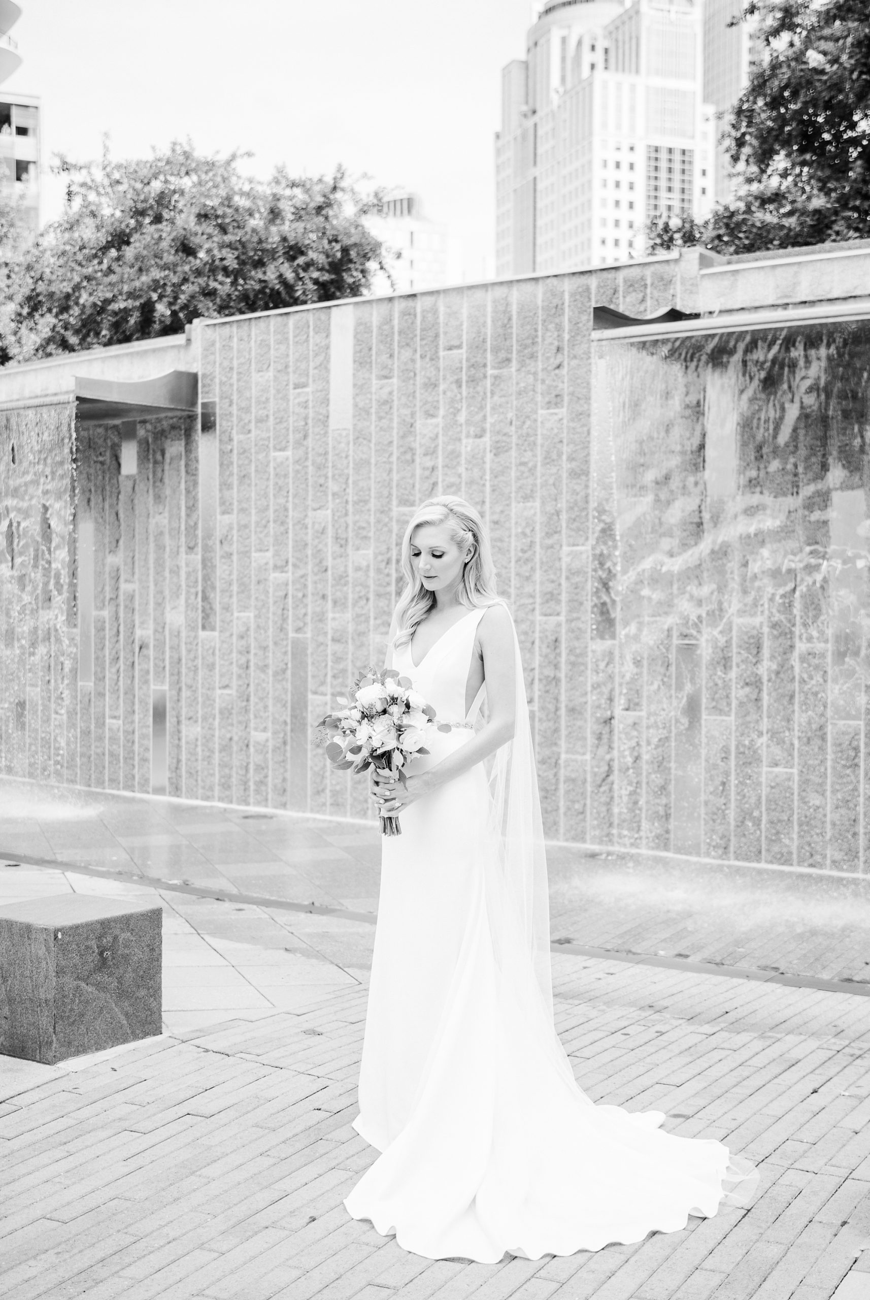 black and white bridal portrait of bride looking down at bouquet by waterfall in Romare Bearden Park