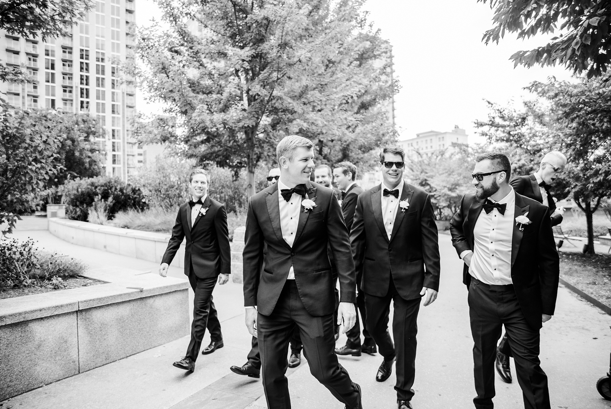groom laughs with groomsmen walking through Romare Bearden Park