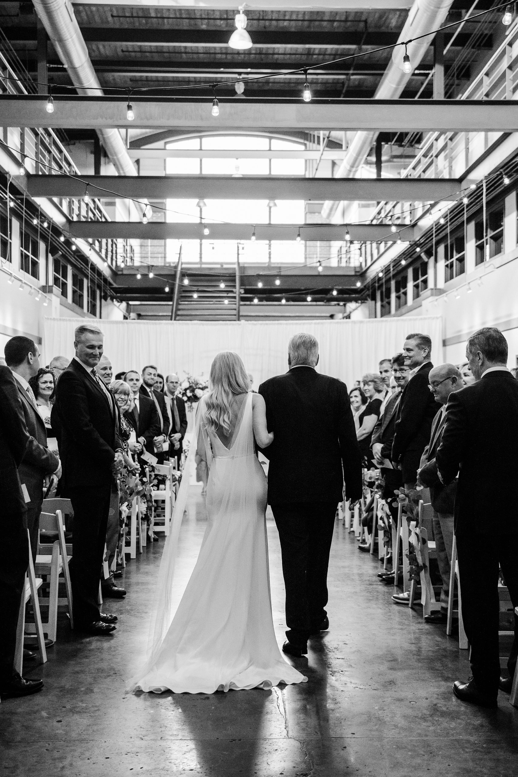 bride walks down aisle with dad at Design Center Atrium