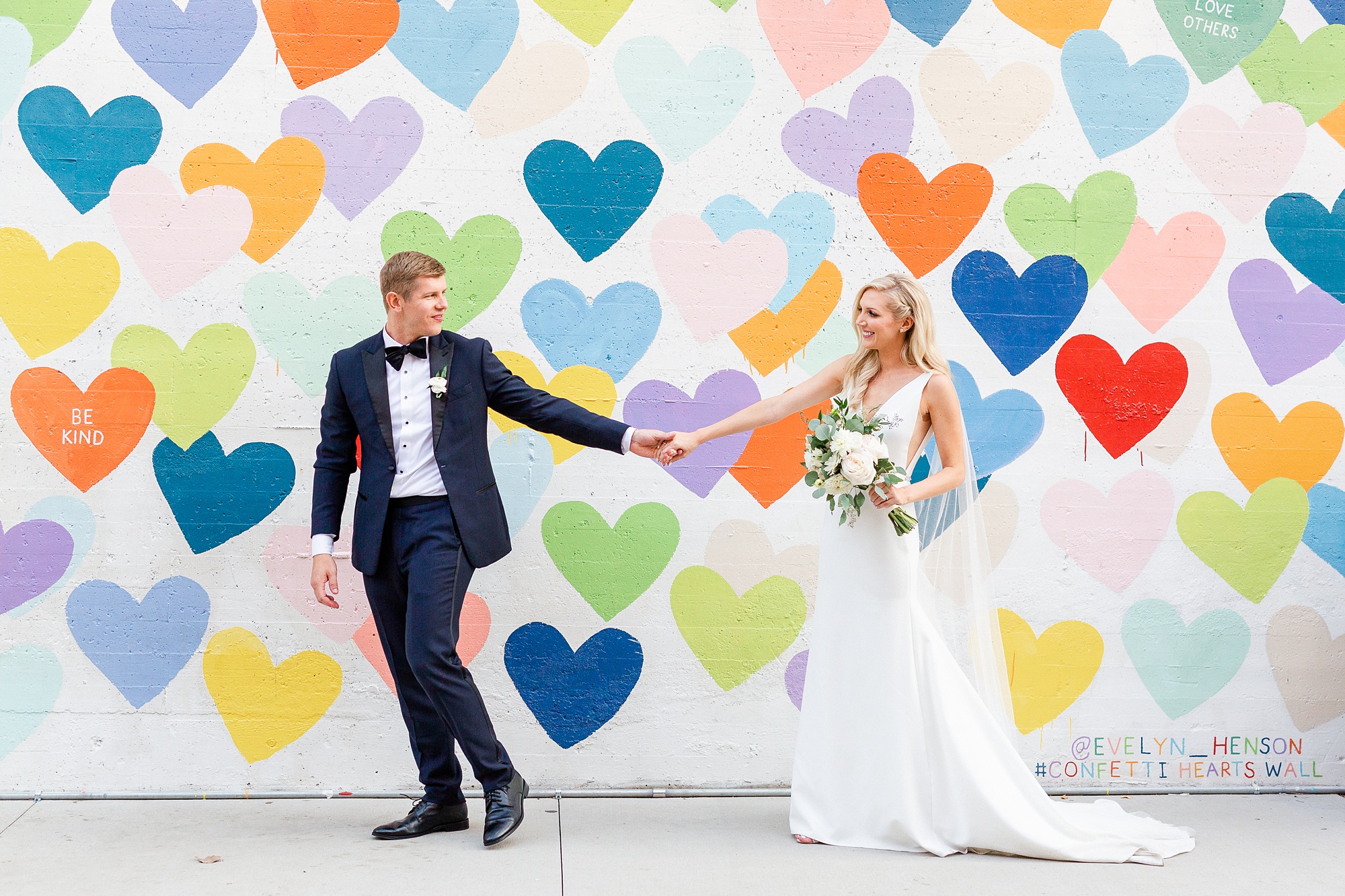 newlyweds hold hands walking by heart mural in uptown Charlotte