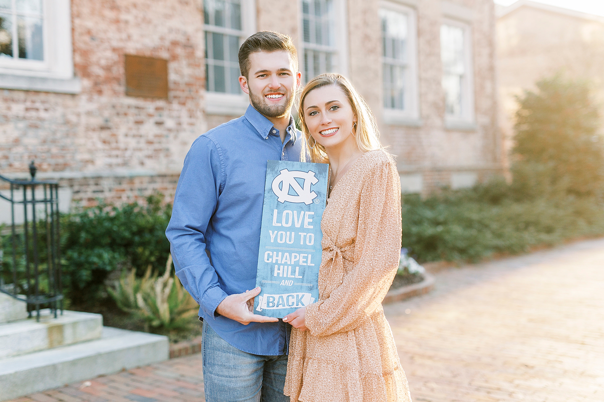 engaged couple holds UNC sign